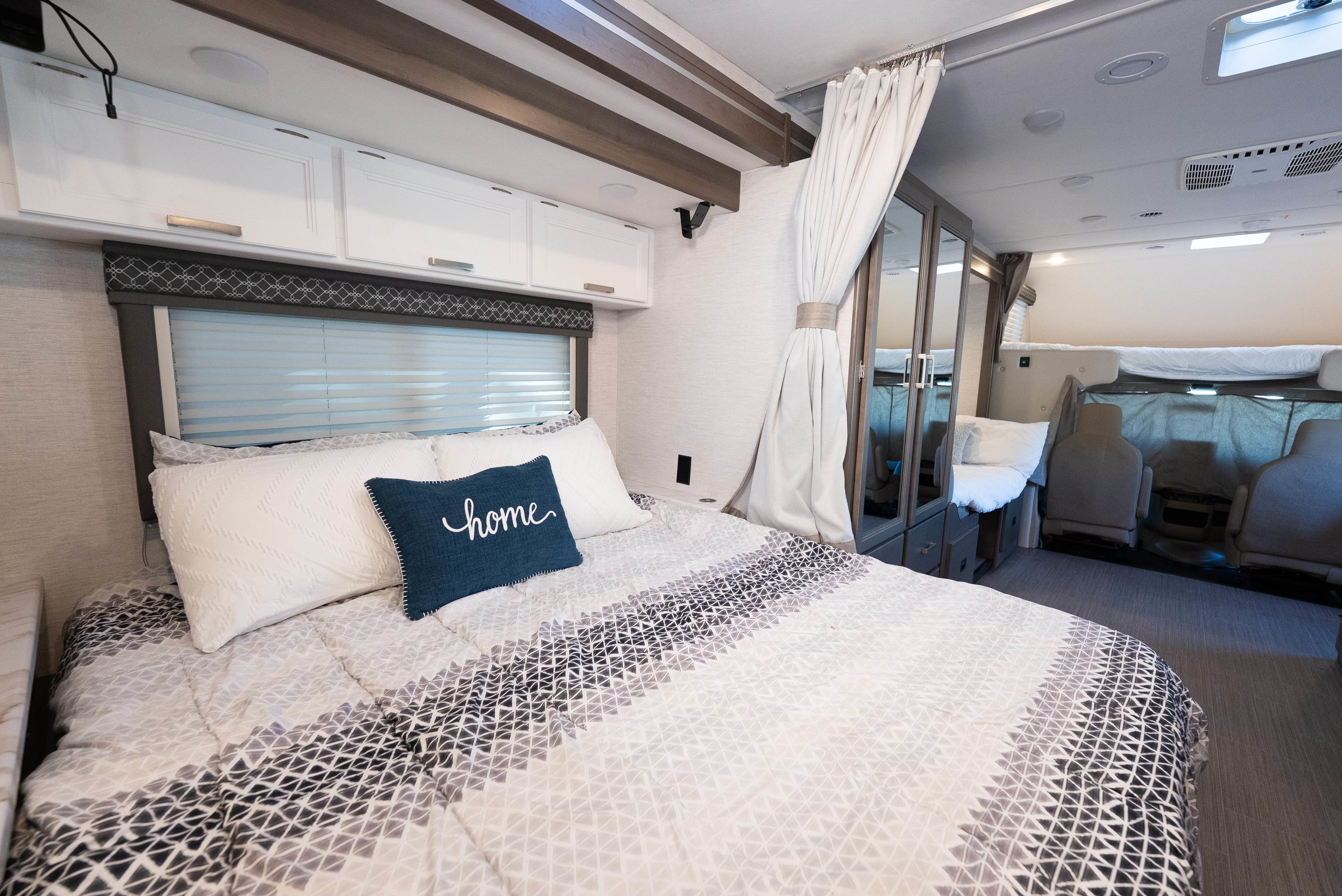 This inviting RV rental bedroom features a comfy bed with a "home" pillow, overhead cabinets, and a space-saving design.. Thor Freedom Elite 2025