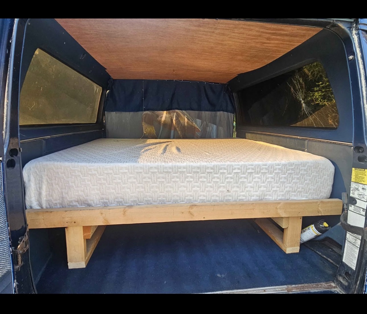 DIY camper conversion for rv rental: a cozy bed platform with a mattress inside a truck topper, blue carpeted floor.. Chevrolet G-20 1983