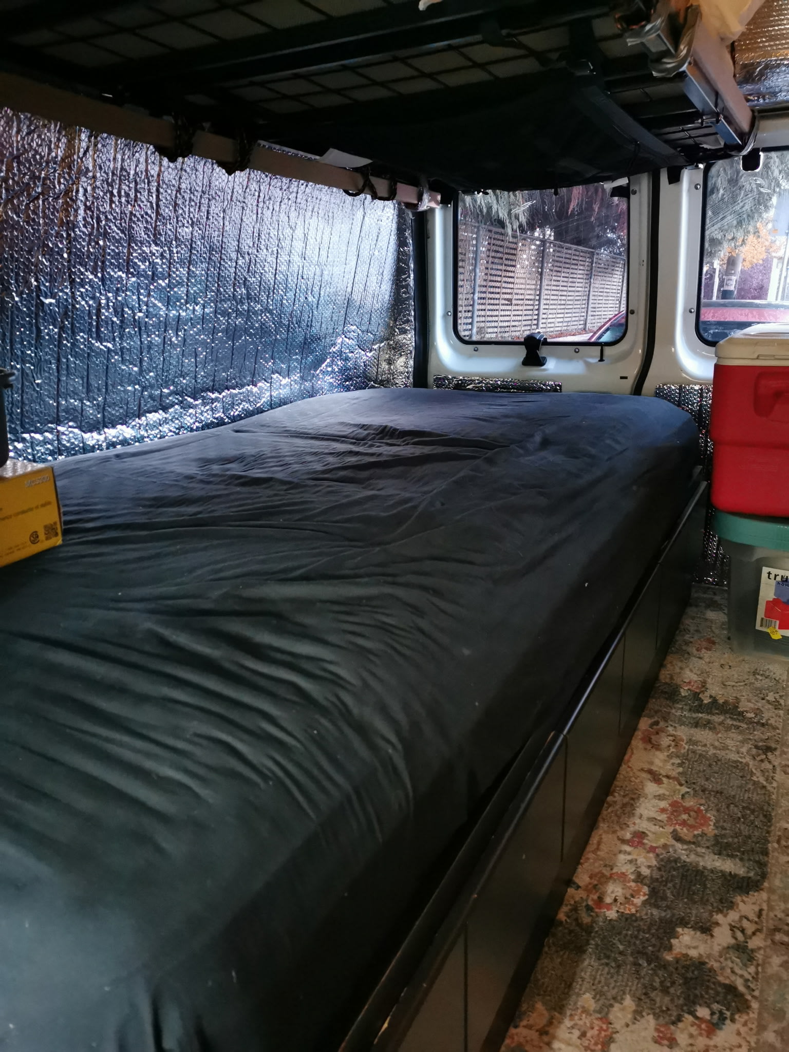 Inside an RV rental: a neatly made bed, reflective insulation on walls, and storage options like a cooler.. Ford Econoline 150 1992