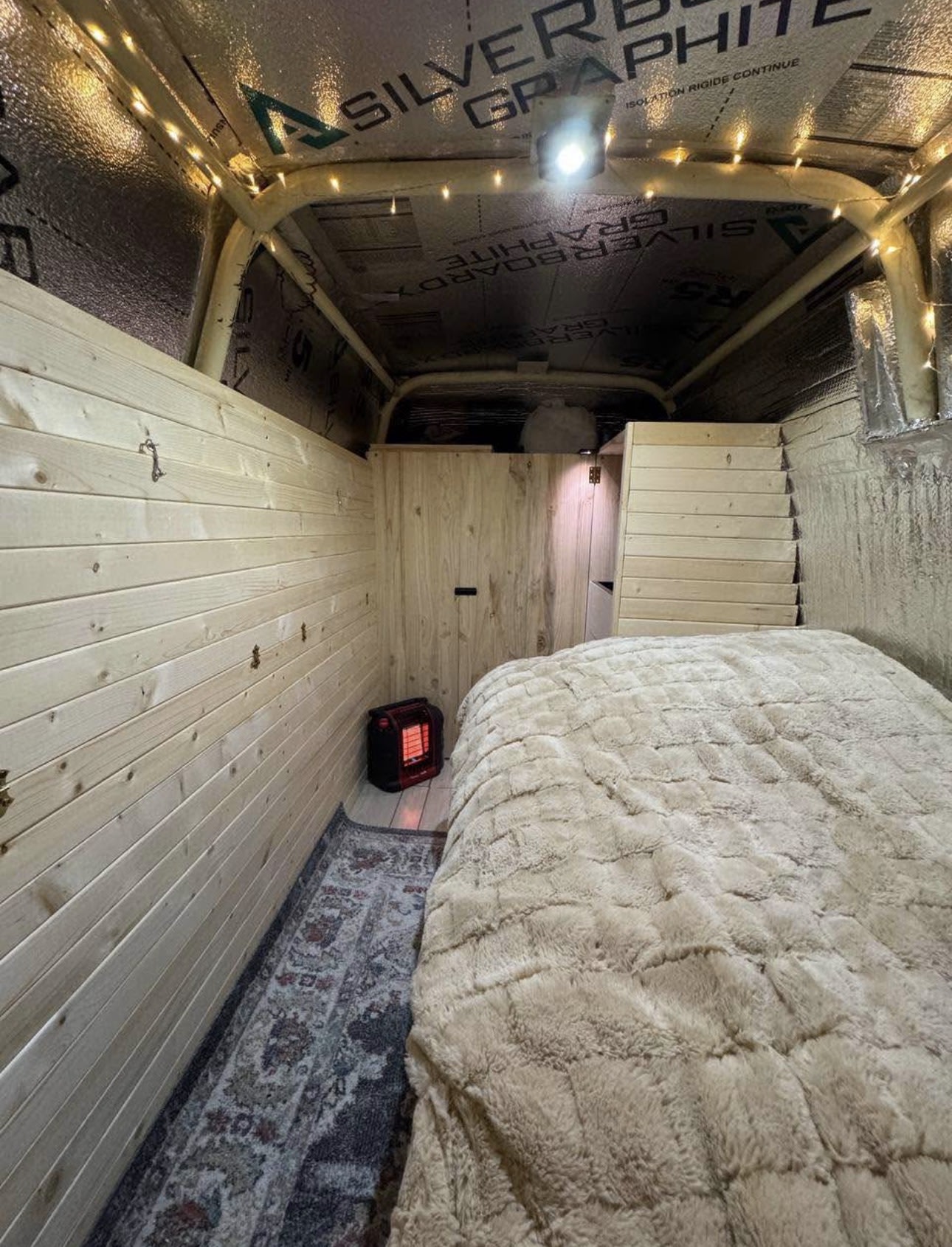 This cozy rv rental interior features wood walls, a plush bed, rug, and heater, perfect for comfortable van life.. Ford Econoline 150 1992
