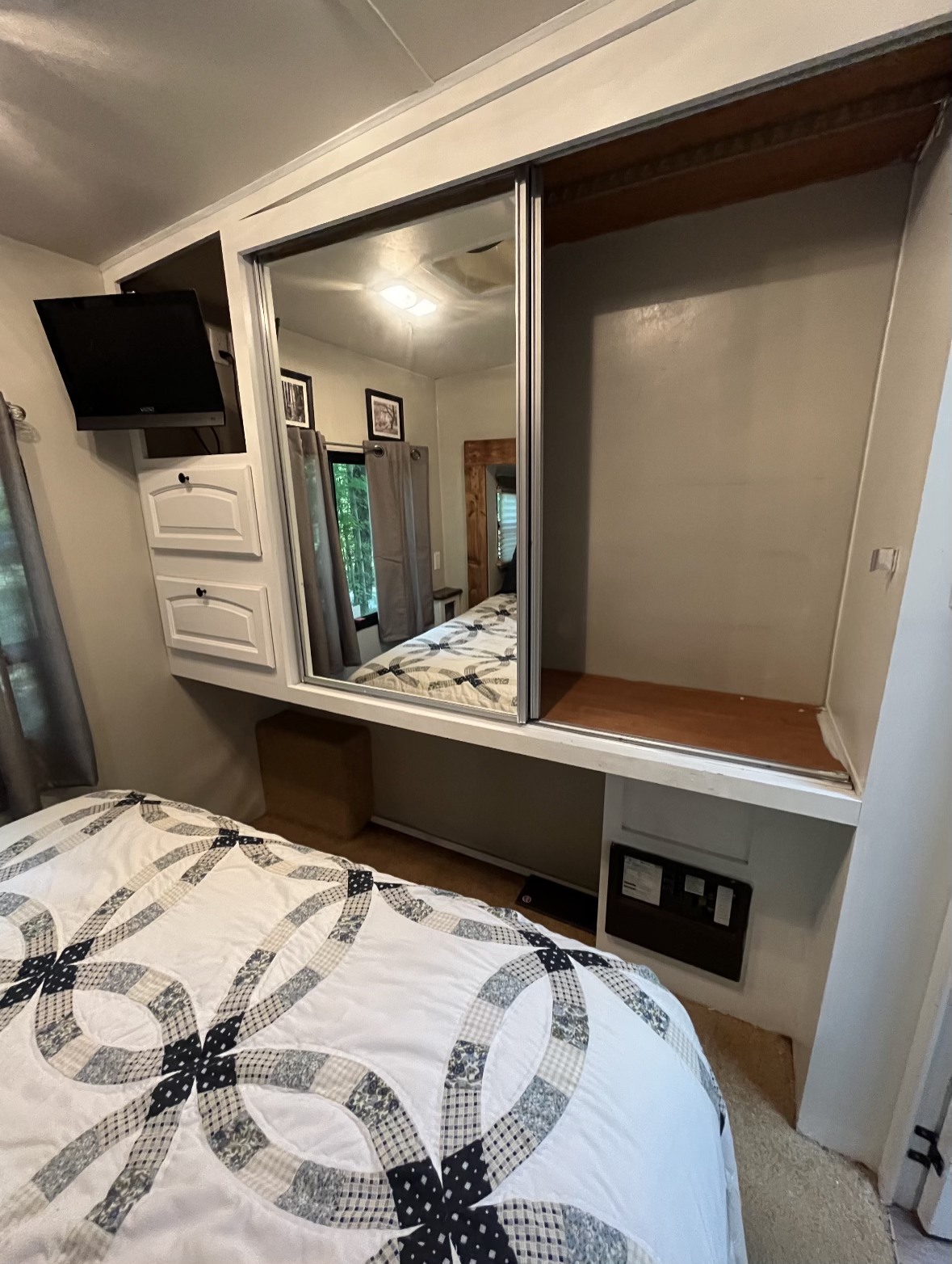 Cozy RV rental bedroom features a built-in mirror closet, wall-mounted TV, and storage drawers over a patterned bed.. Forest River Wildcat 2011
