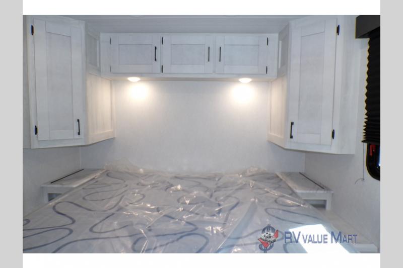 This RV rental bedroom features a bed with overhead cabinets, side shelves, and lighting for comfortable stays.. East to West Entrada 2026