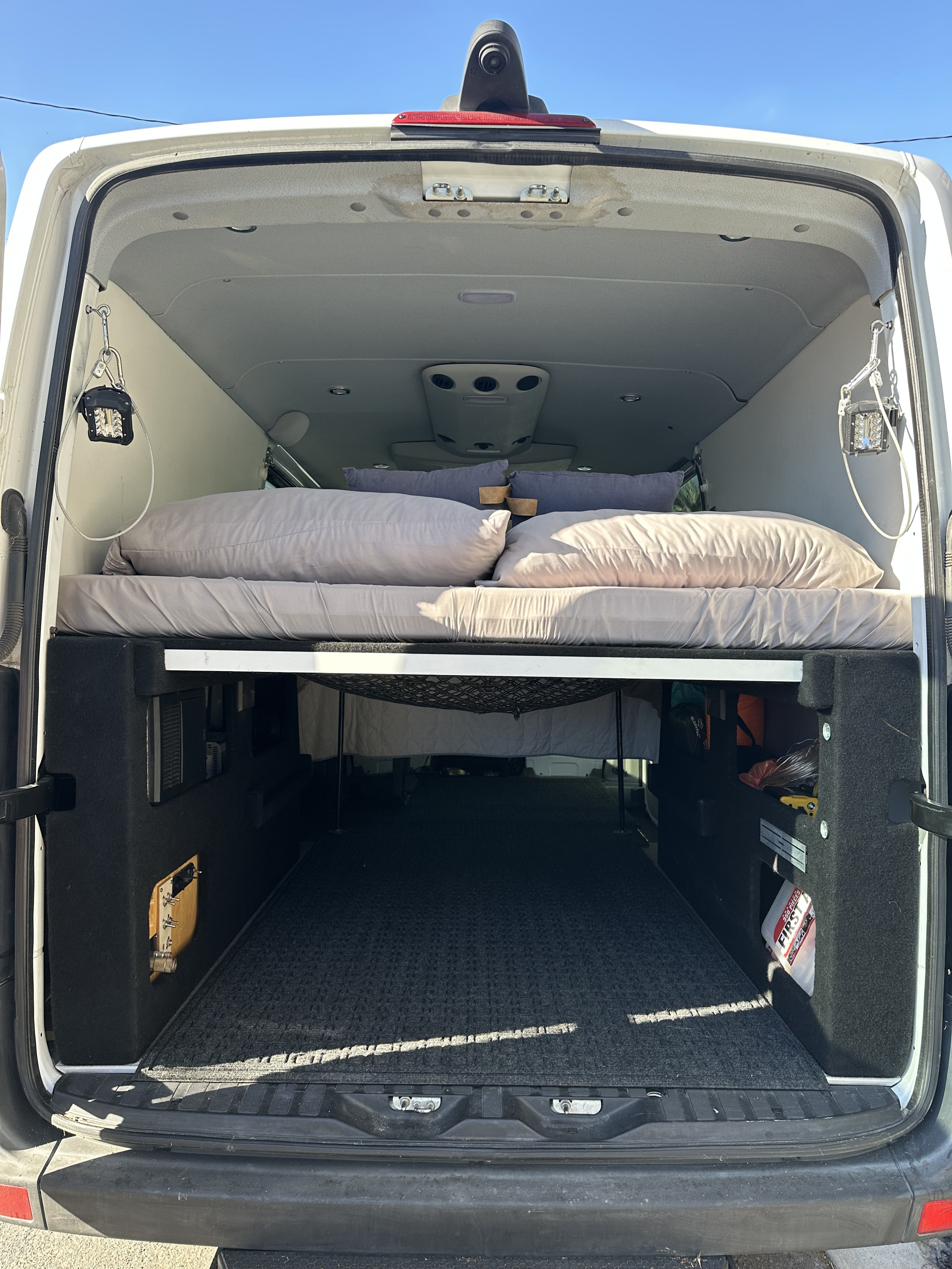 RV rental camper van interior. Elevated bed platform with pillows, spacious under-bed storage, and utility lights.. Mercedes-Benz Sprinter 2014