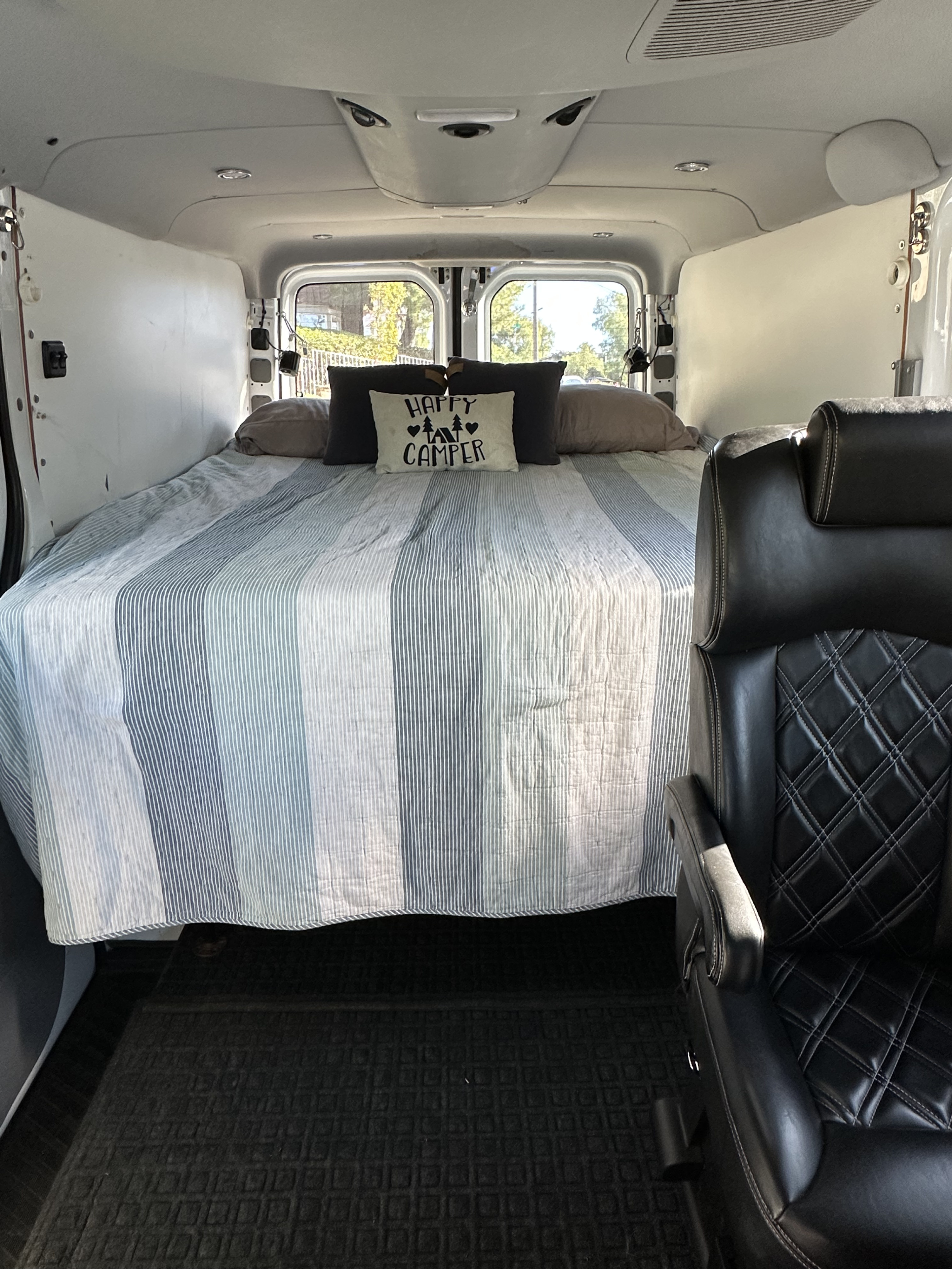 RV rental: Cozy camper van interior featuring a comfortable bed with a "Happy Camper" pillow and a black leather seat.. Mercedes-Benz Sprinter 2014
