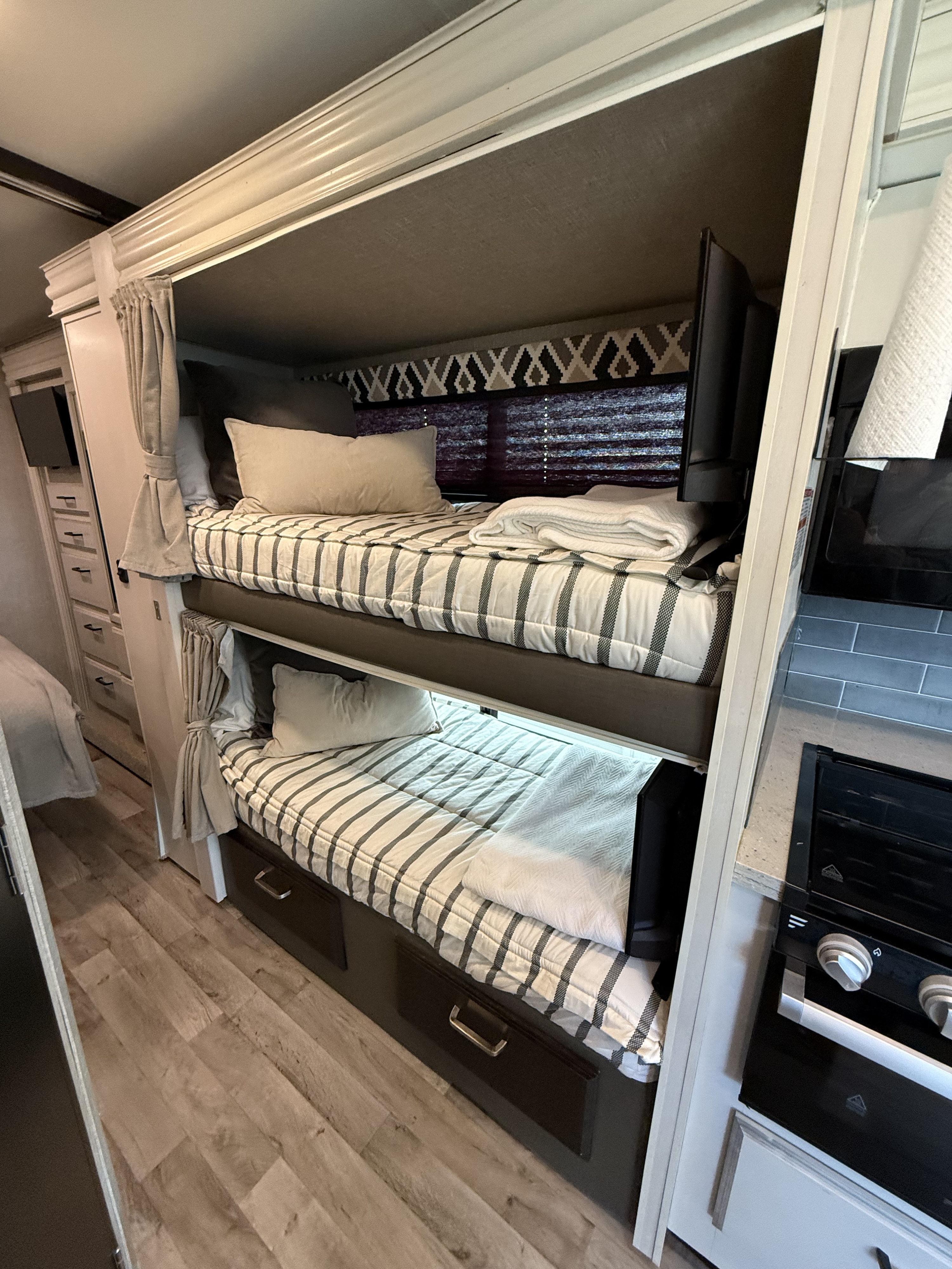 Cozy bunk beds in an RV rental, complete with striped bedding, a small TV, and storage drawers, perfect for compact living.. Entegra Coach Odyssey 2022