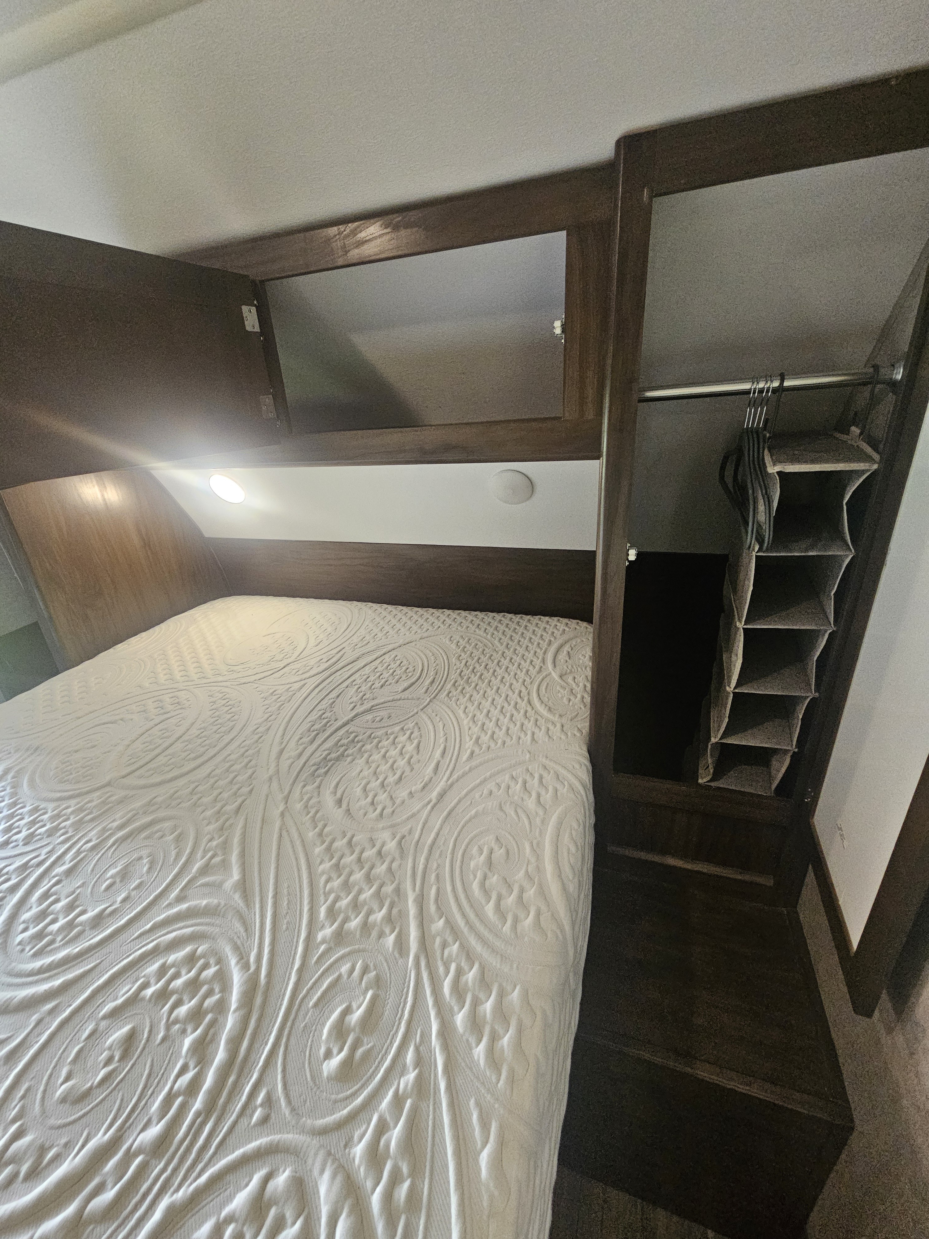 Comfortable RV rental bedroom featuring a white patterned mattress, overhead storage, and a small closet with an organizer.. Forest River Cherokee 2018