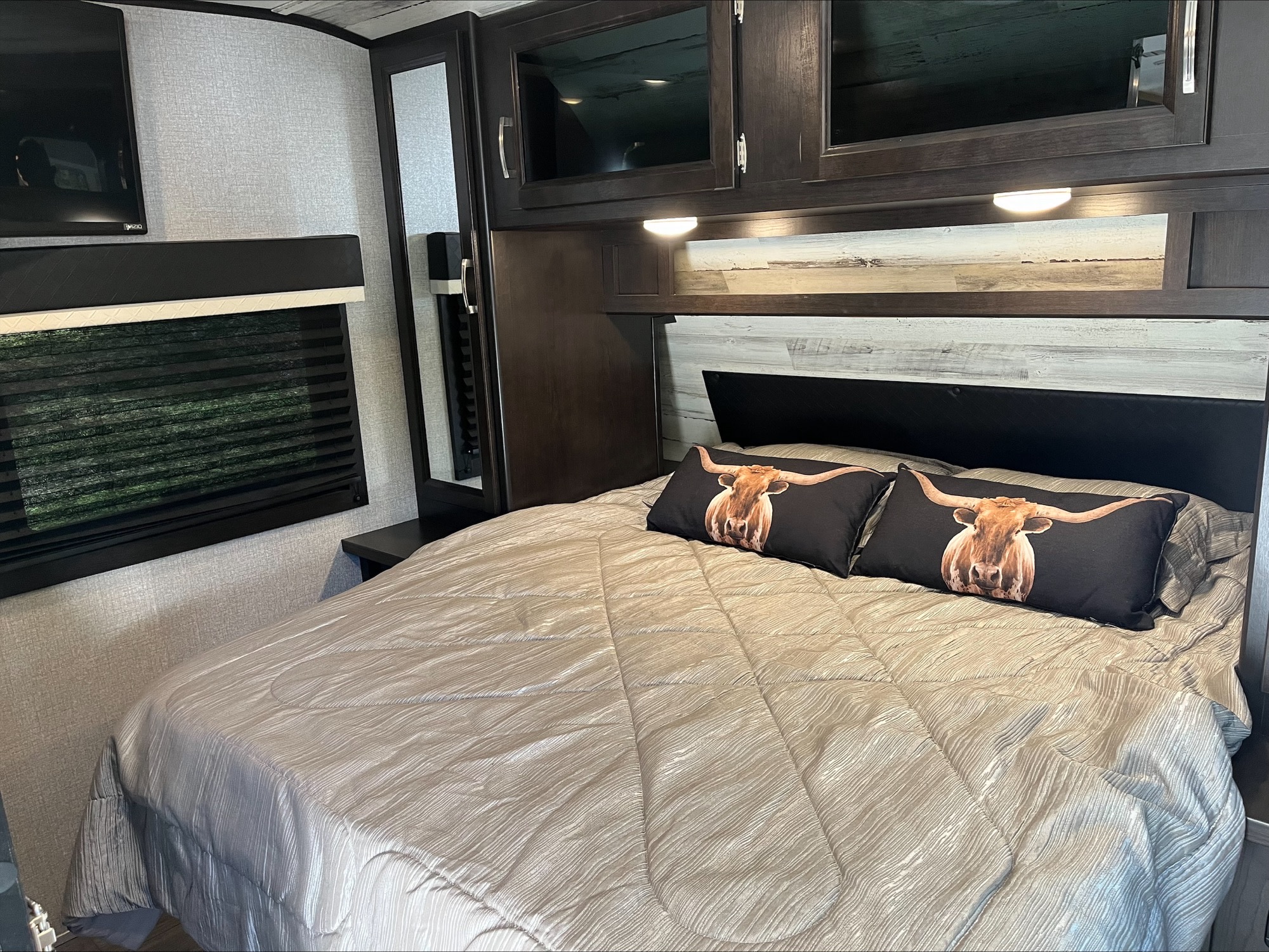 Comfortable RV rental bedroom with a plush bed, rustic headboard, longhorn pillows, TV, and overhead storage.. Jayco Jay Feather 2021