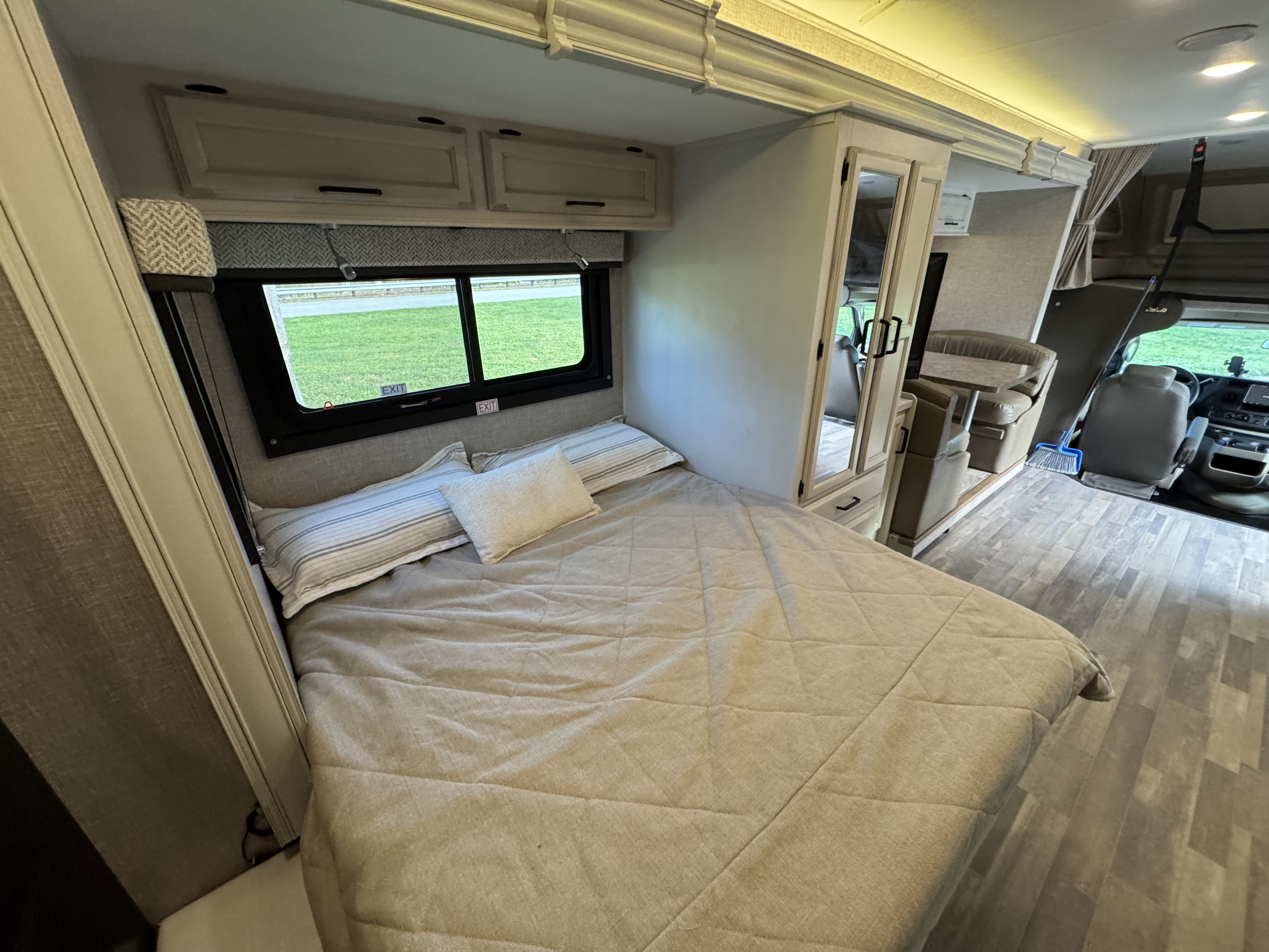 Inside an rv rental, a bedroom features a made bed, window with green view, overhead cabinets, and a mirrored closet.. Entegra Coach Odyssey 2023