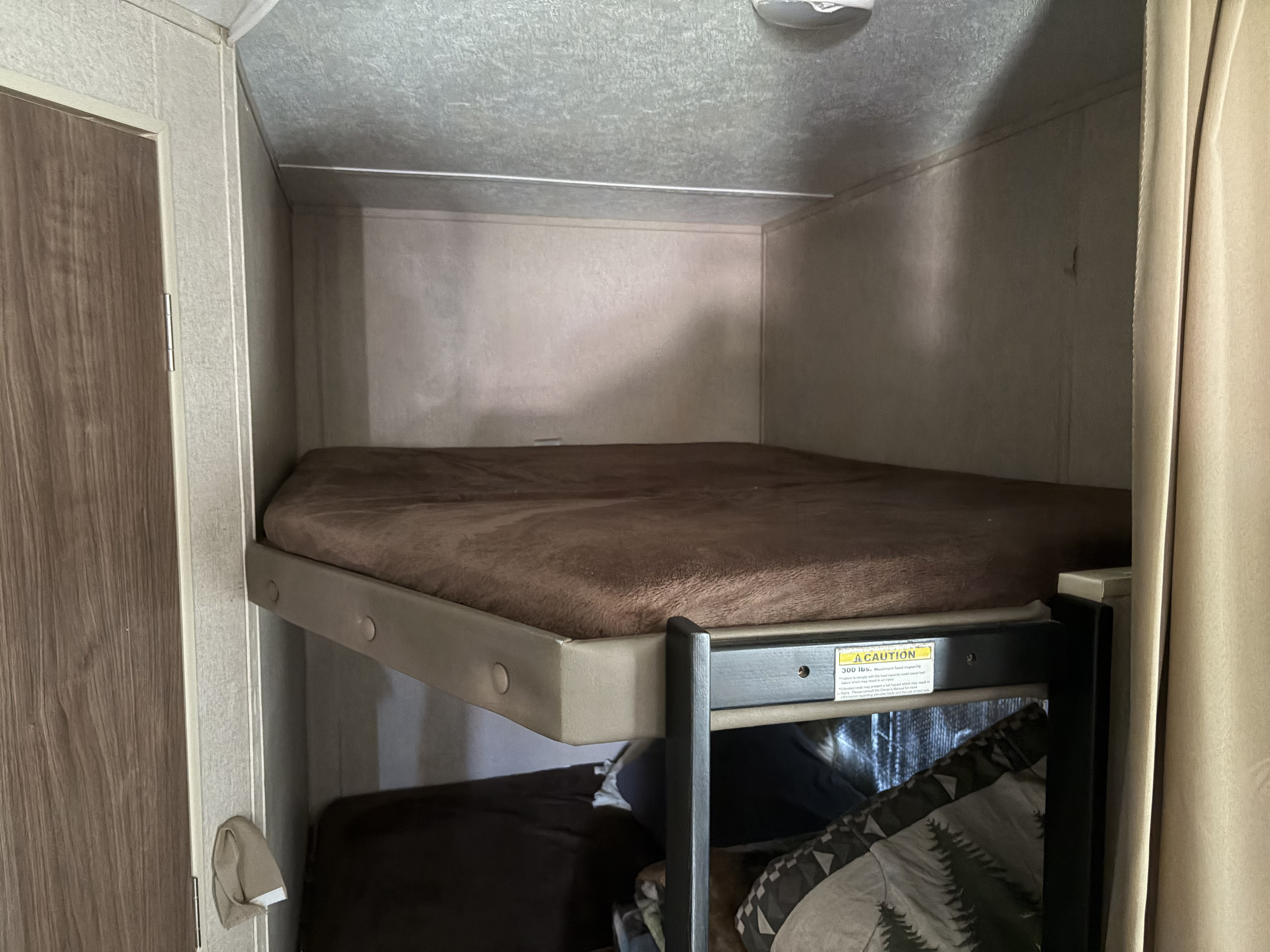 Cozy RV rental bunk beds with a brown fuzzy mattress on the top bunk, featuring a 300 lb weight limit.. Dutchmen Coleman Lantern 2018