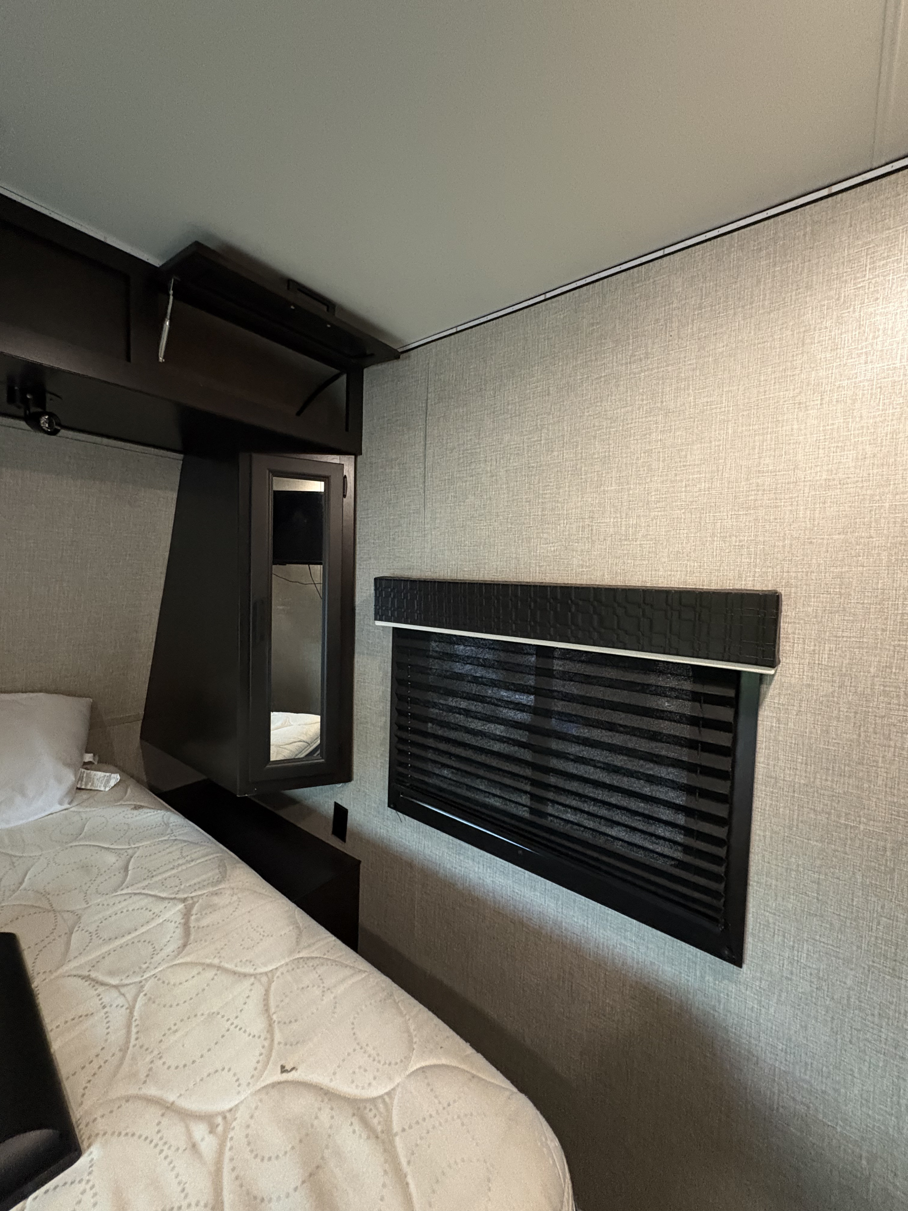 Experience comfort in this RV rental bedroom: featuring a quilted mattress, dark wood storage, and a privacy blind.. Jayco Jay Flight 2022