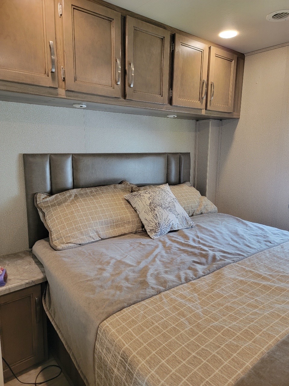 Cozy RV rental bedroom featuring an upholstered headboard, comfortable bed, and practical overhead storage cabinets.. Entegra Coach Vision 2019