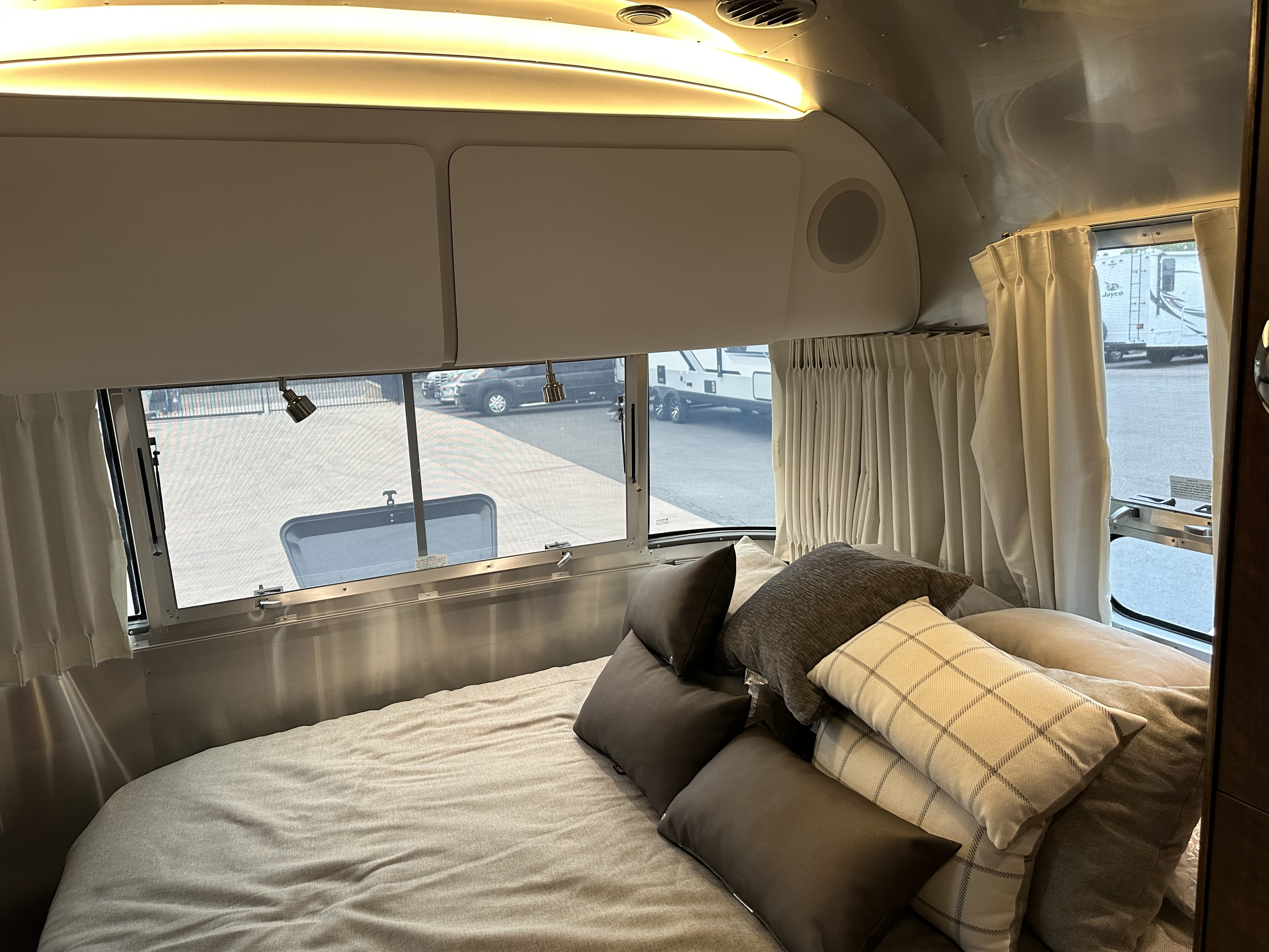 Experience comfort in this RV rental's bedroom, featuring a plush bed, multiple pillows, and panoramic window views.. Airstream Globetrotter 2020
