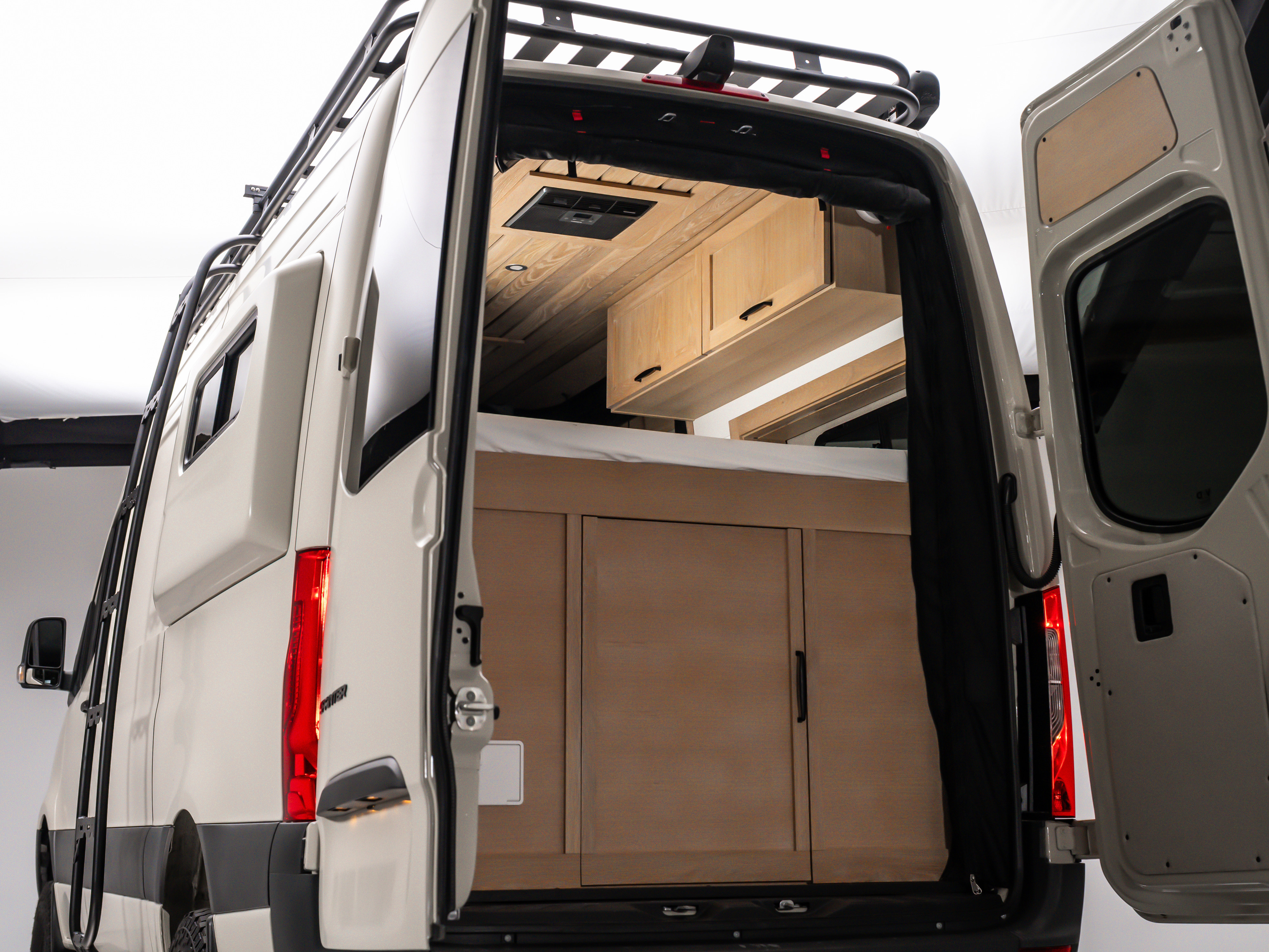 Rear view of a spacious RV rental interior with custom wooden cabinetry, bed, and ventilation, perfect for journeys.. MERCEDES-BENZ Sprinter 2500 2024