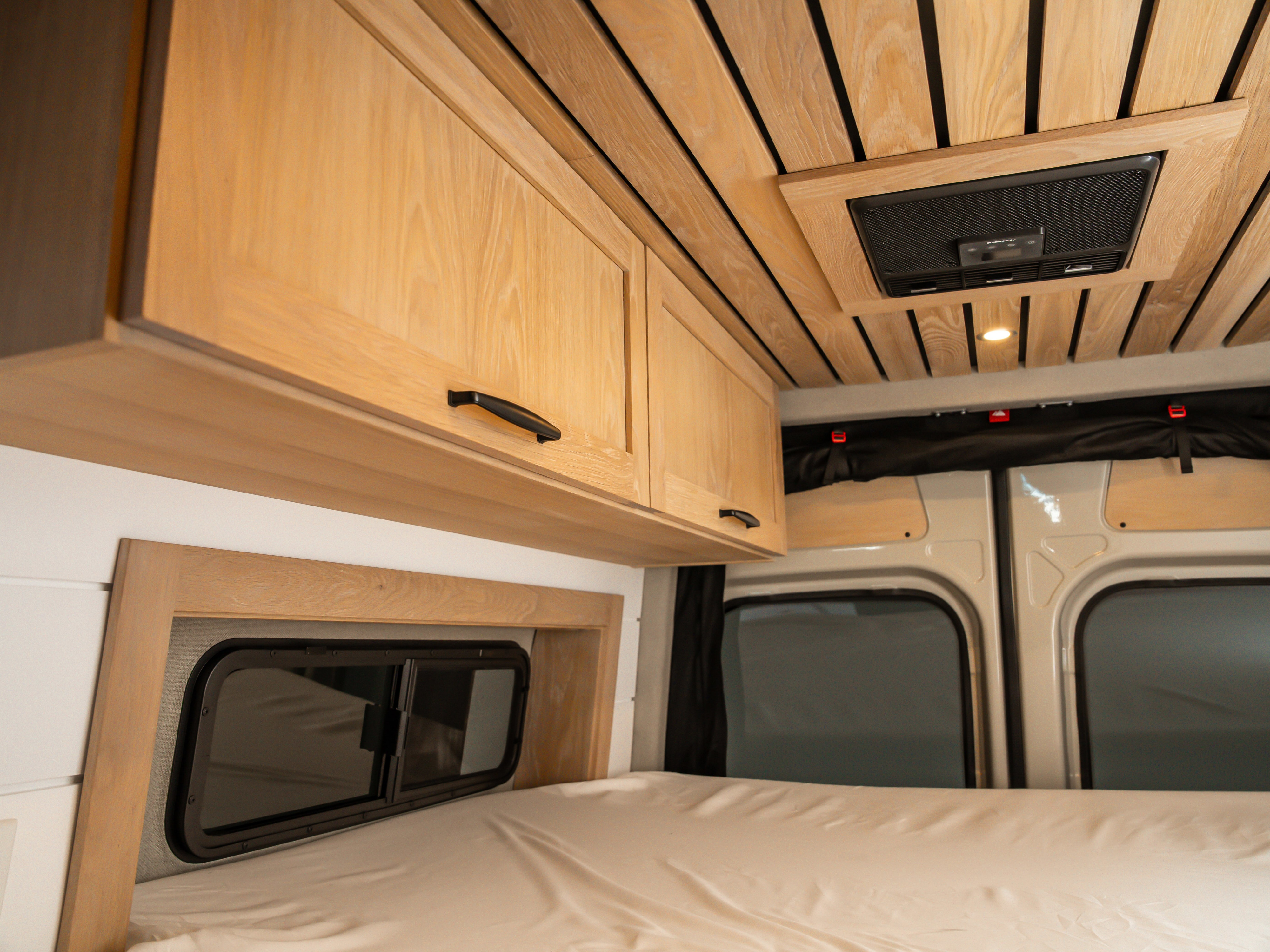 Inside an RV rental: light wood cabinets, slatted ceiling with vent, cozy bed, and side windows.. MERCEDES-BENZ Sprinter 2500 2024