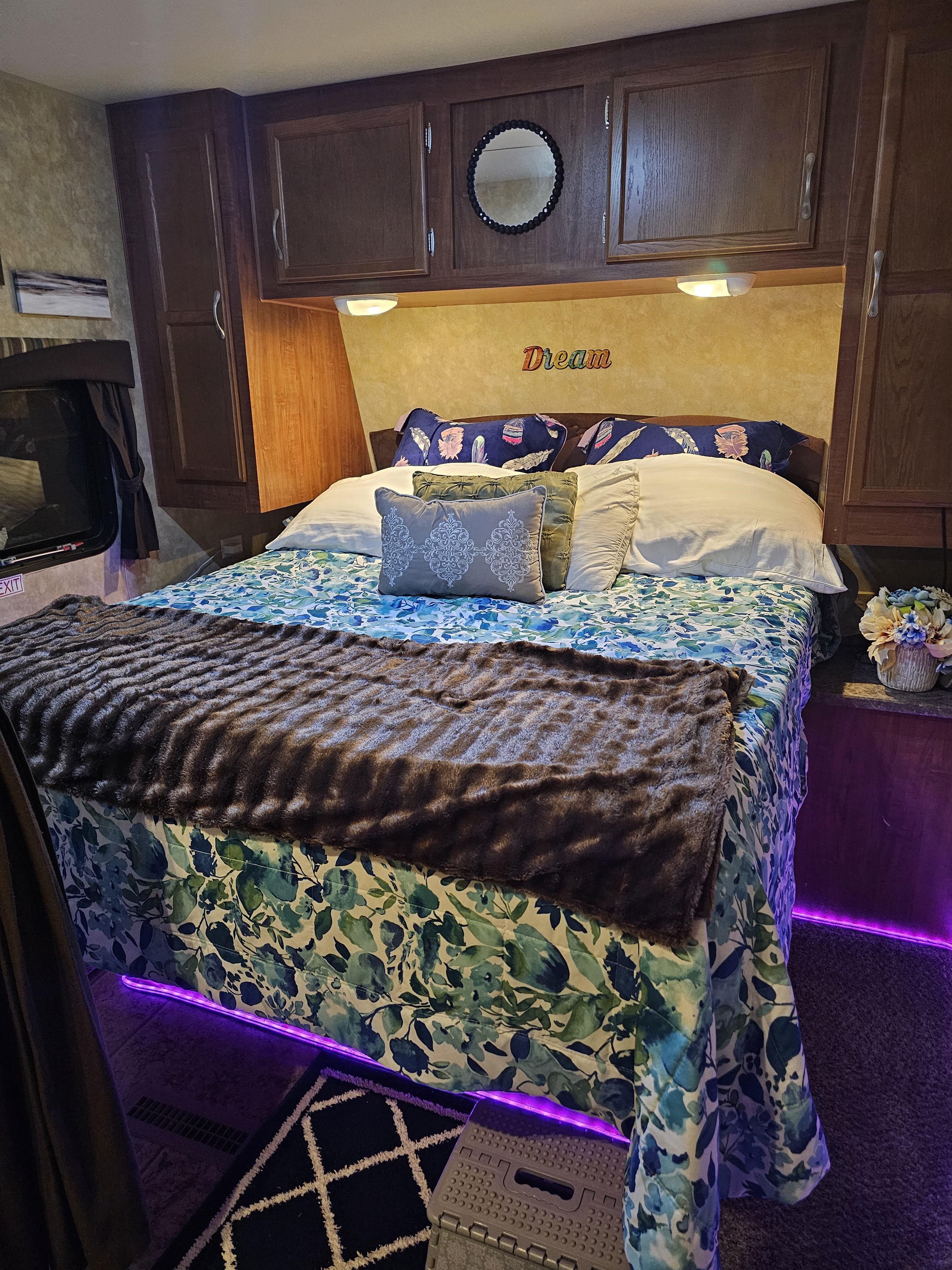 RV rental bedroom: floral bed, faux fur, purple accent lights. Dark wood cabinets & 'Dream' sign create a cozy, inviting space.. Jayco Jay Flight 2010