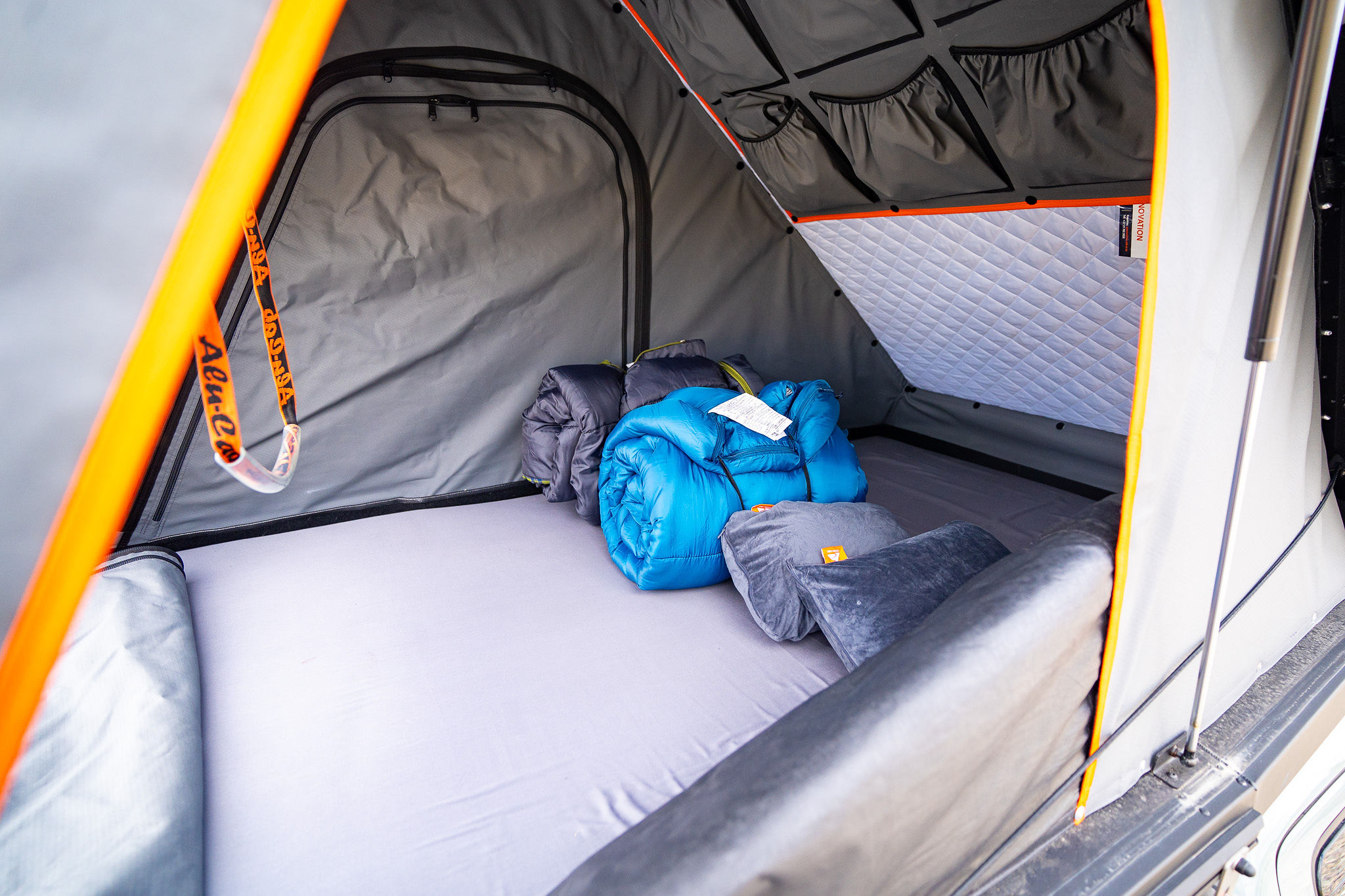 Inside a comfy Alu-Cab rooftop tent for rv rental. Features a mattress, rolled sleeping bags, pillows, and wall storage.. Toyota Tacoma TRD Expedition 2020