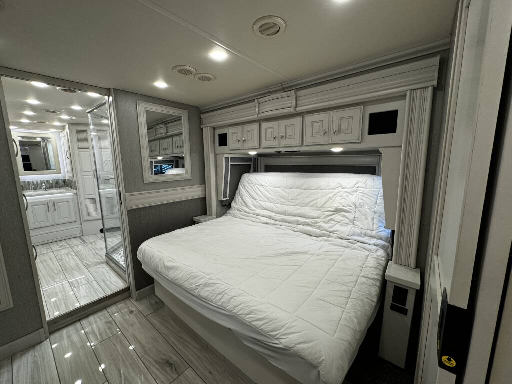 Inside a modern rv rental: a cozy bedroom with a large bed, overhead storage, and an adjacent stylish bathroom.. Holiday Rambler Armada 2022