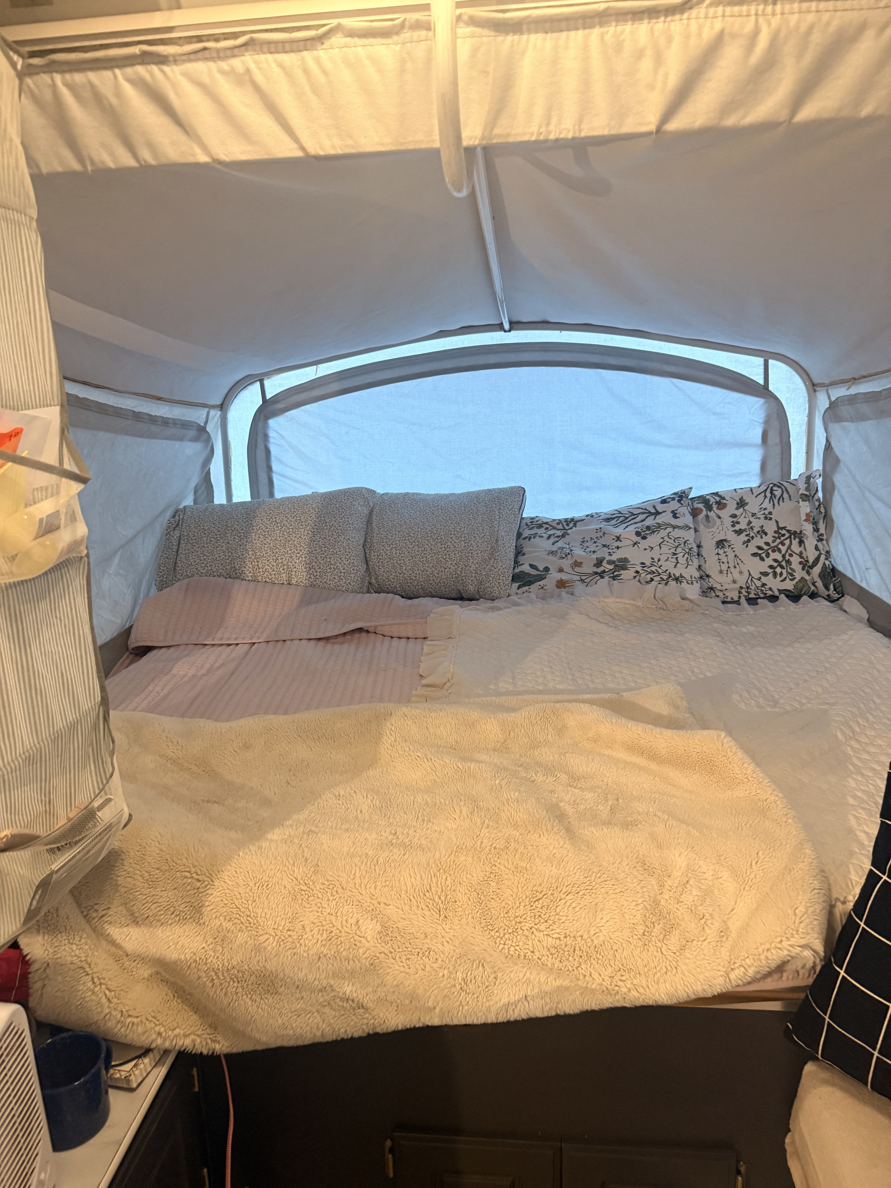Inside a cozy rv rental, a pop-up camper bed features patterned pillows, soft pink sheets, and a fluffy beige blanket.. Coleman Grand Tour 2002