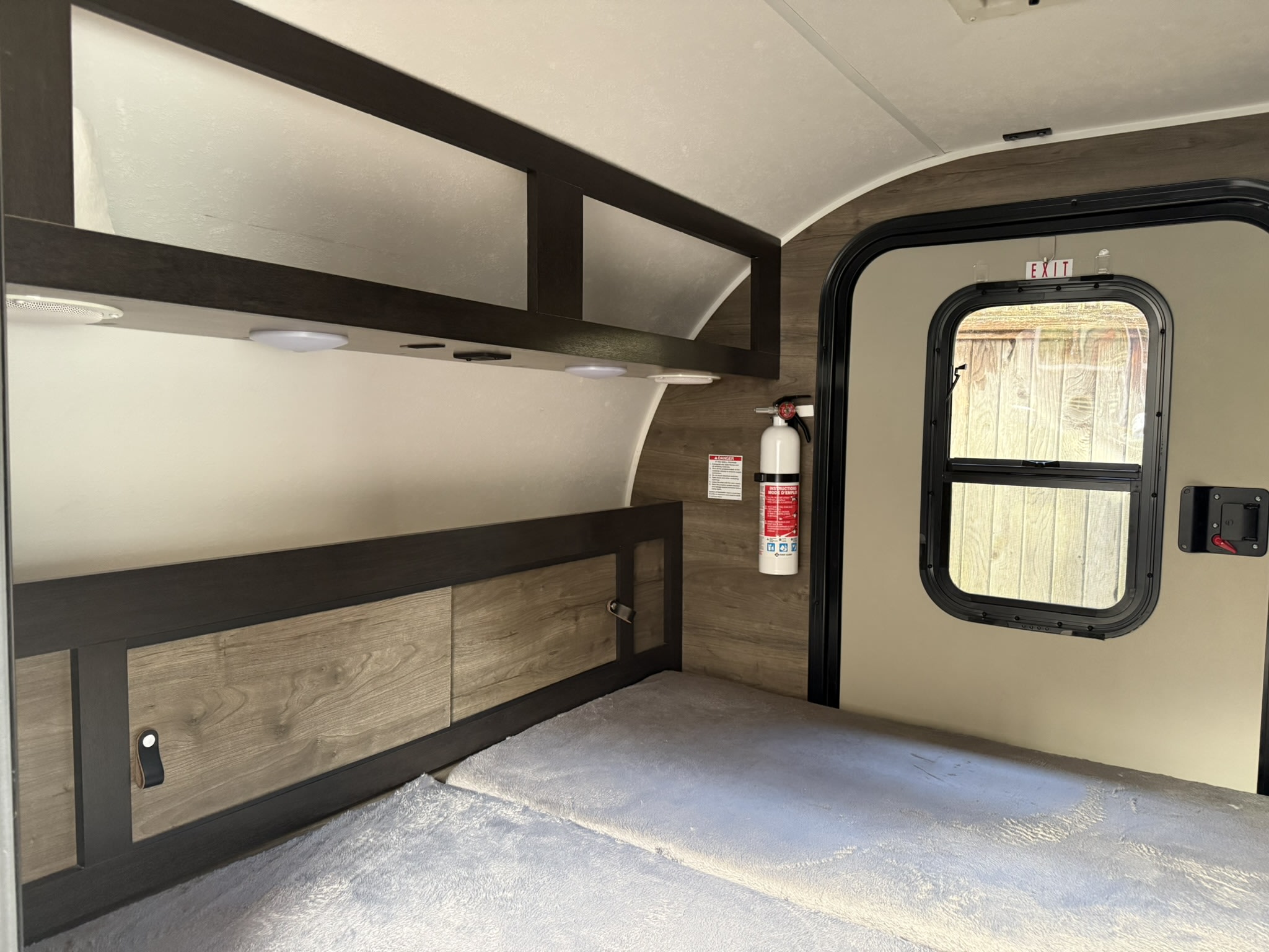 RV rental bedroom area showing a bed, wood-paneled walls, overhead storage, exit door, and a fire extinguisher.. Braxton Creek Bushwhacker 2022