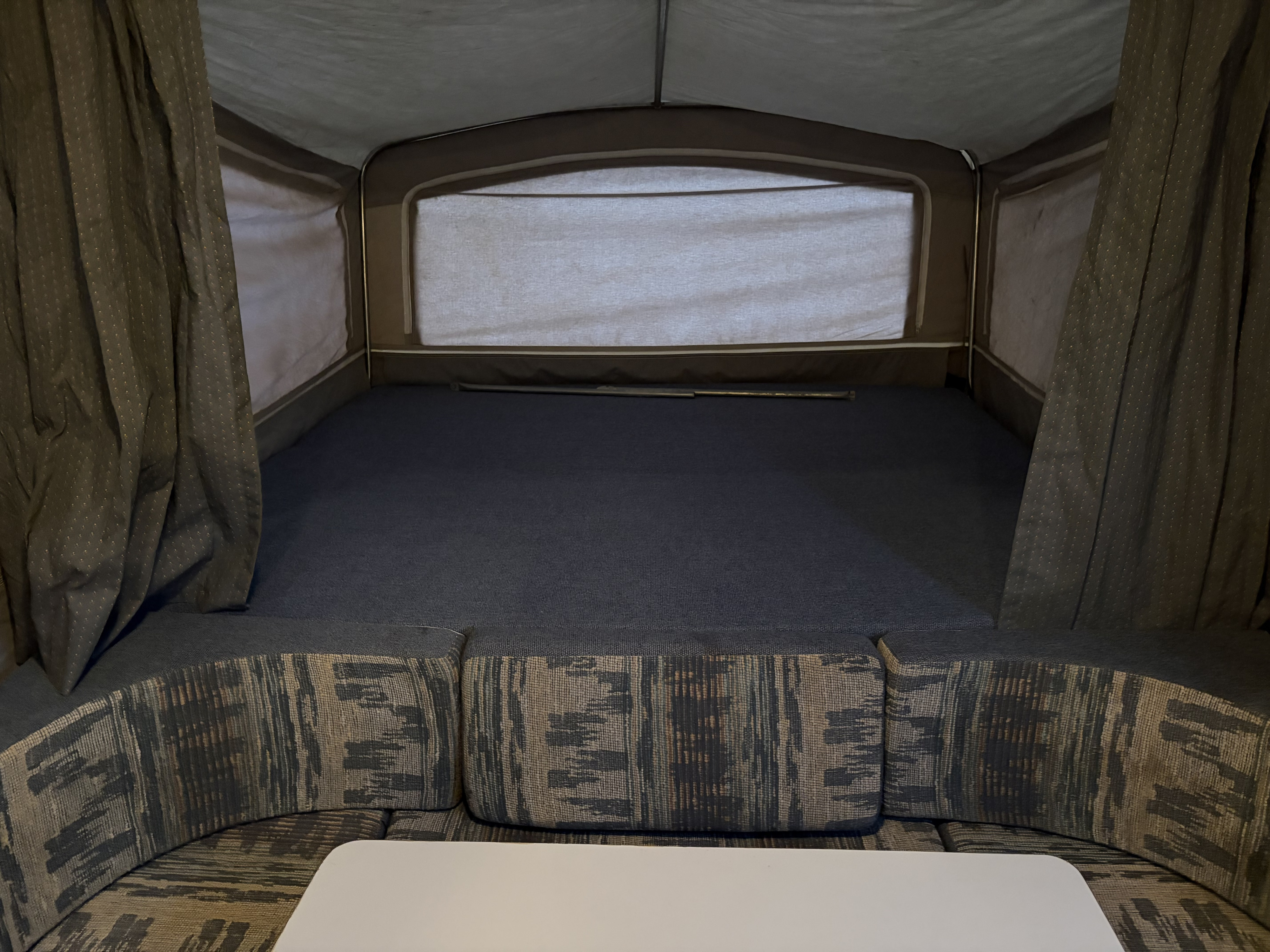 Relax in this RV rental's pop-up camper interior: comfy bed, patterned dinette seating, and table for your adventure.. Dutchmen M1204 1996