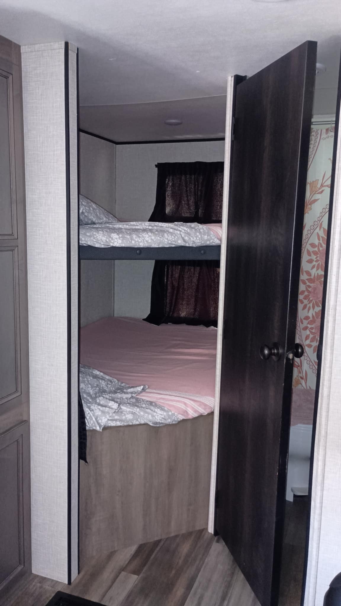 RV rental: Bunk beds with pink & gray patterned bedding in a cozy sleeping area. An open door reveals the RV bathroom.. Starcraft Autumn Ridge 2024