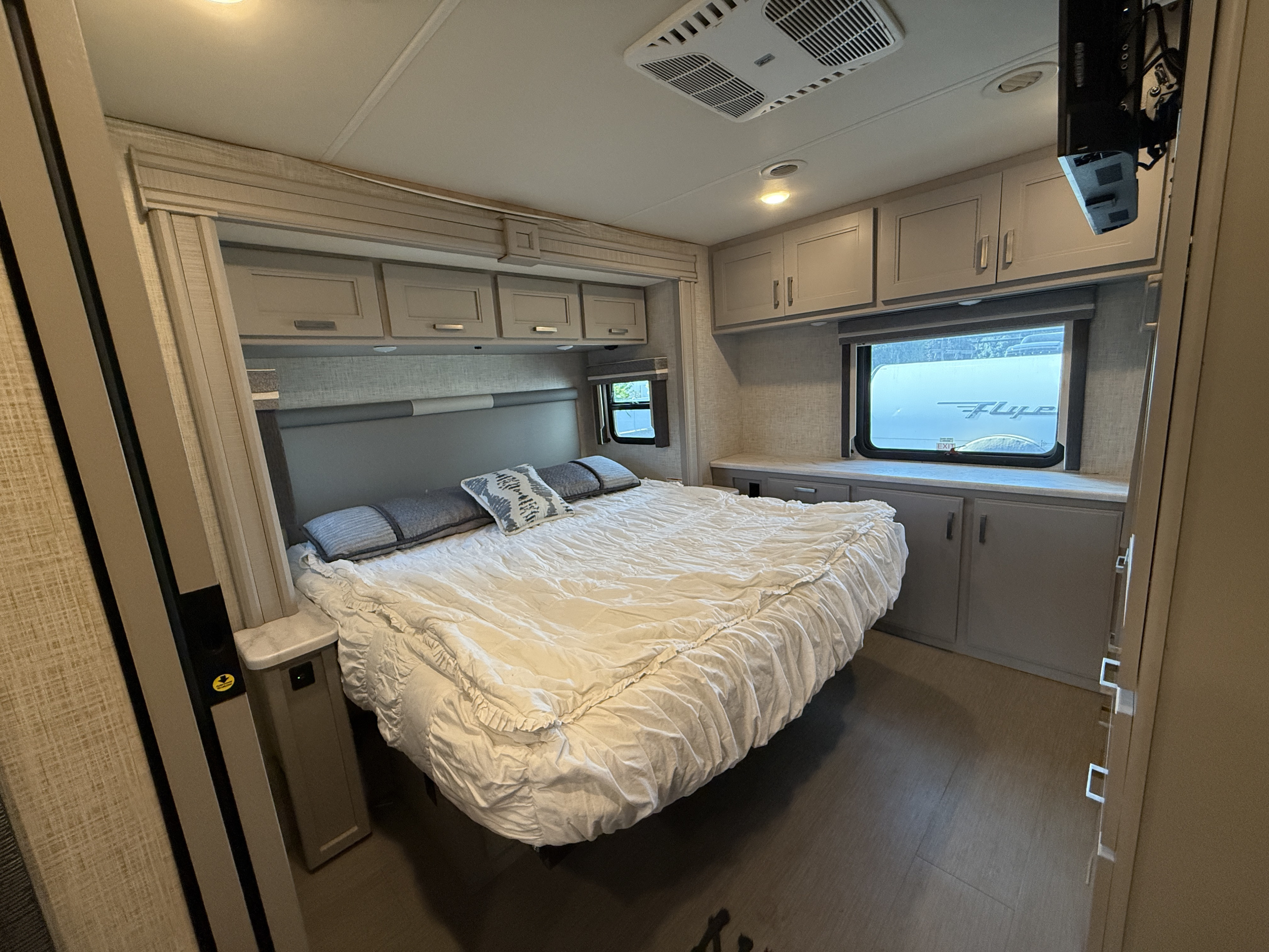 Modern RV rental bedroom with a large bed, overhead cabinets, a comfortable headboard, and soft, light gray tones throughout.. Thor Inception 2023
