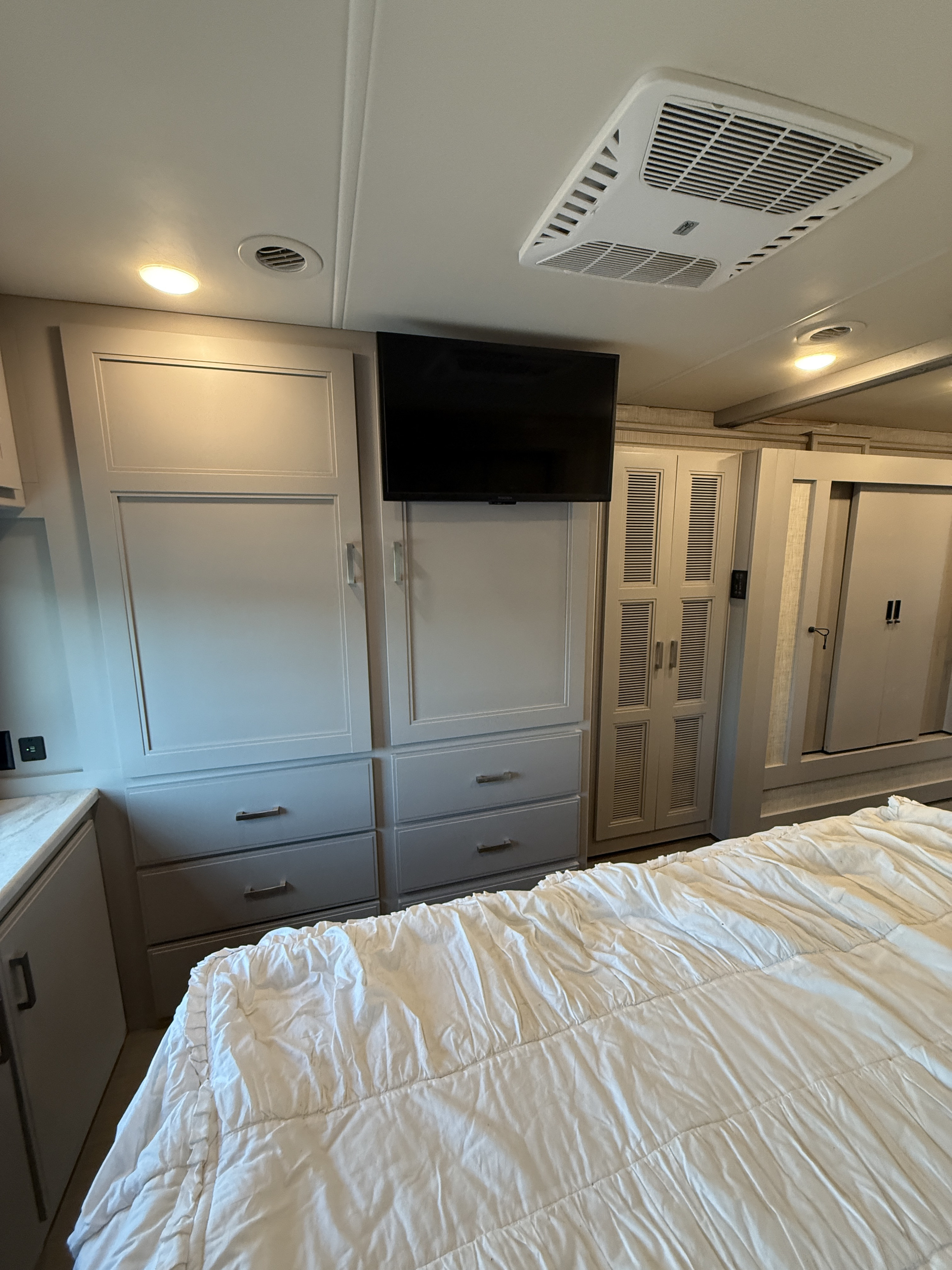 RV rental bedroom with a mounted TV, ceiling AC, and ample built-in cabinetry, featuring a large bed.. Thor Inception 2023