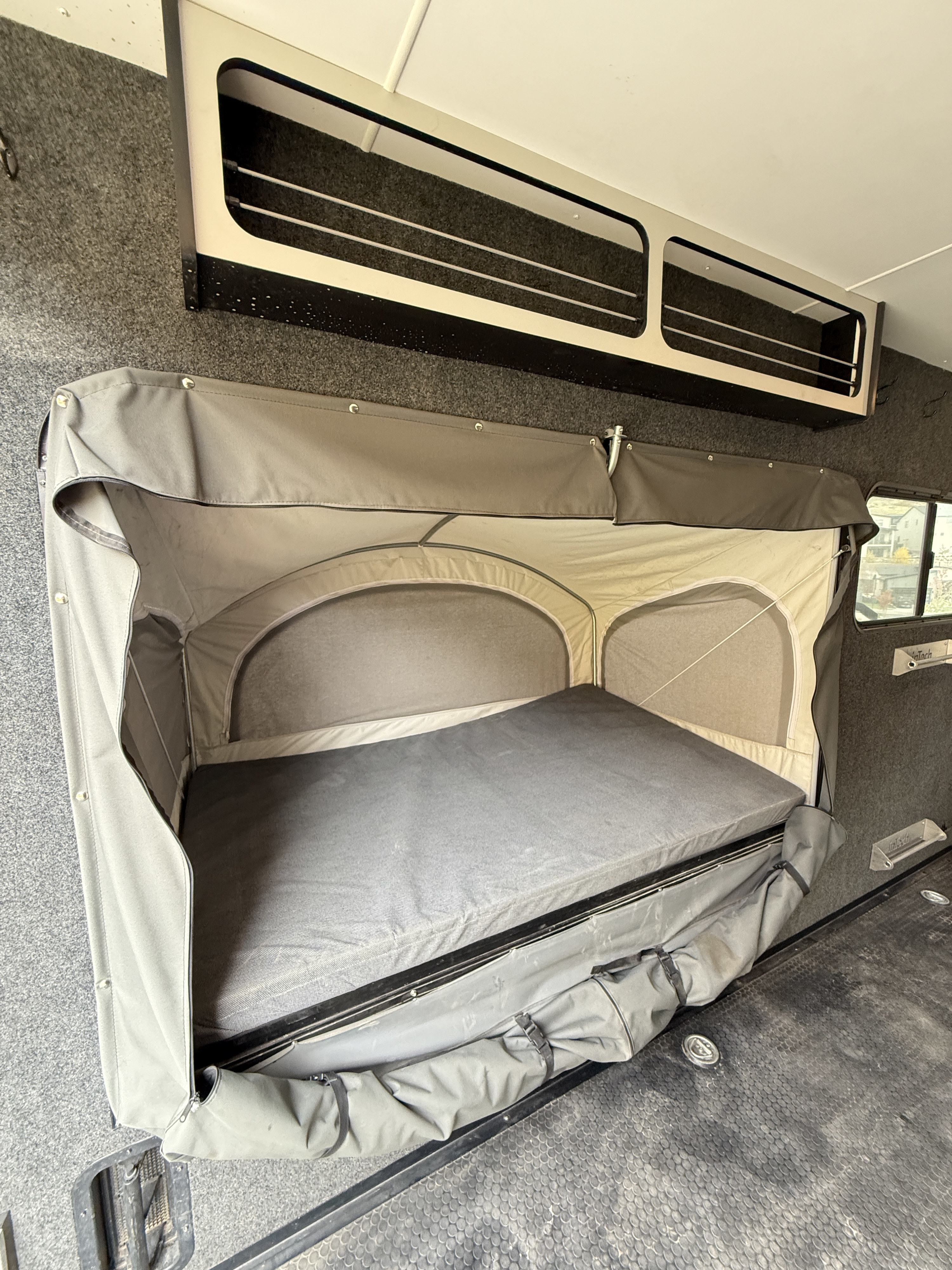 This RV rental shows a unique fold-down sleeping bunk with fabric enclosure, overhead storage, and rugged interior finishes.. InTech RV InTech RV Trailer 2022