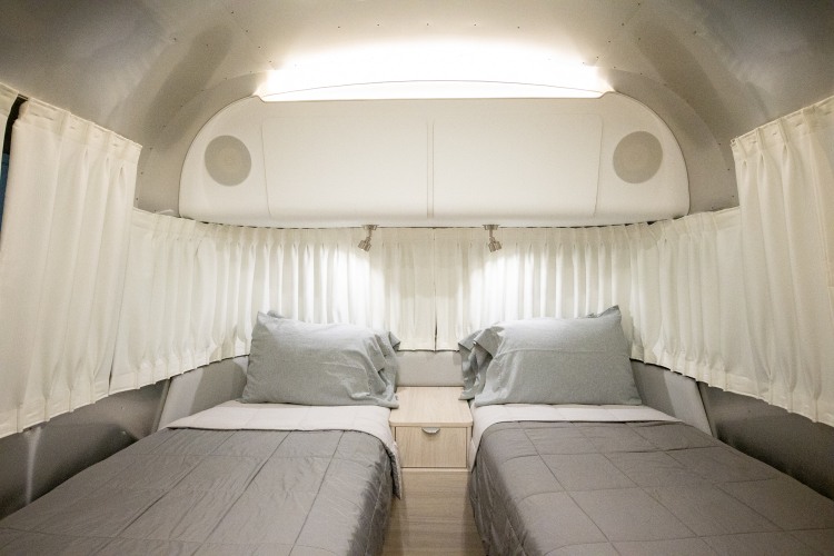 Sleek RV rental bedroom with two twin beds, grey bedding, a nightstand, and reading lights, set in a metallic interior.. Airstream Globetrotter 2022