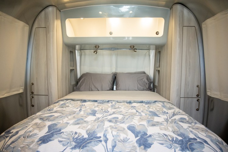 Inside a stylish RV rental, a comfy bedroom features a leafy bed, grey pillows, and sleek built-in storage.. Airstream International 2021