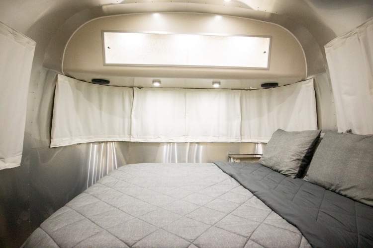 Experience this comfortable rv rental. A cozy Airstream bedroom with a soft bed, privacy curtains, and overhead lighting.. Airstream International 2020