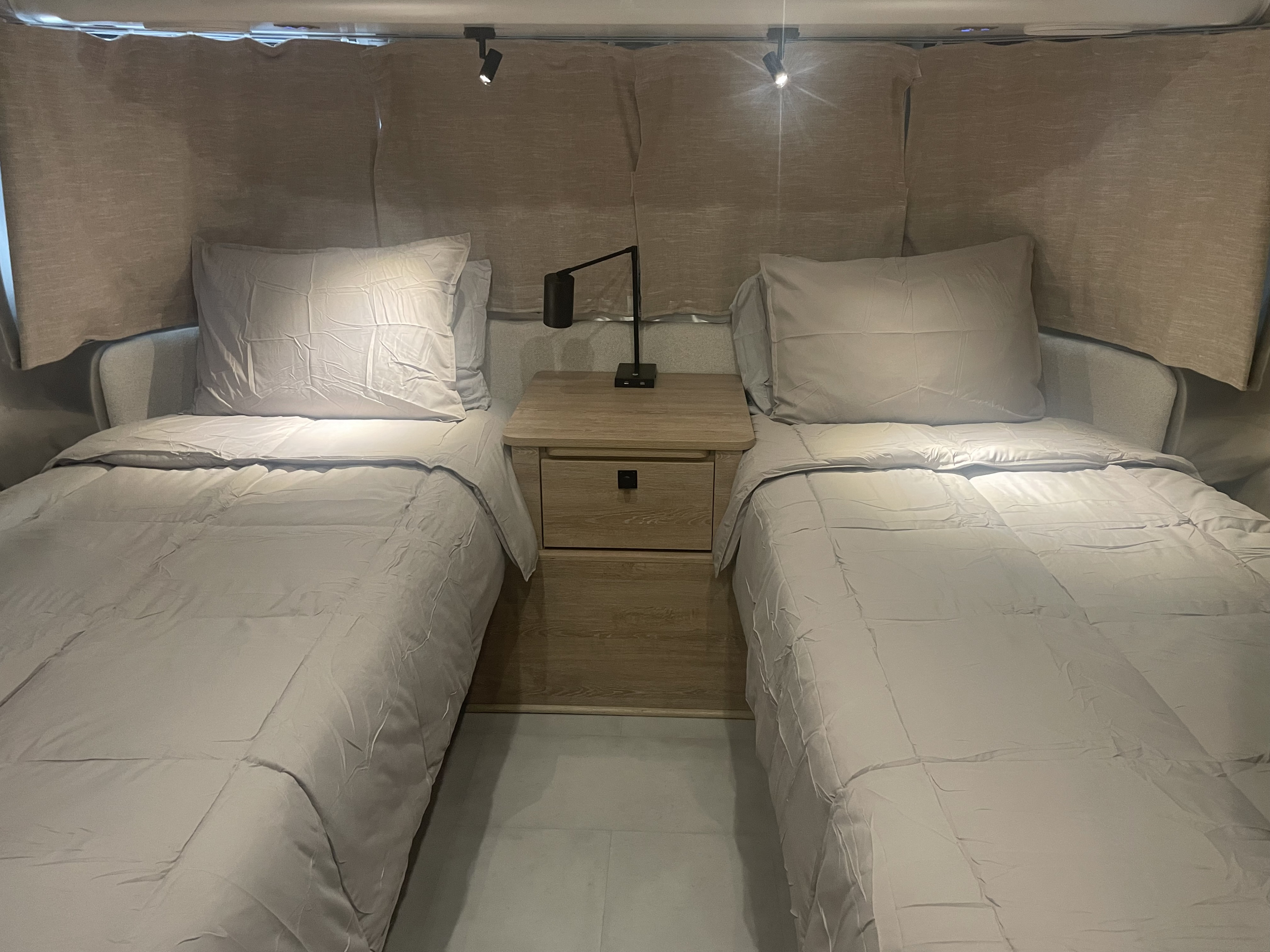 Cozy twin beds in an RV rental, complete with a nightstand and reading lights, perfect for comfortable travel.. Airstream Pottery Barn 2022