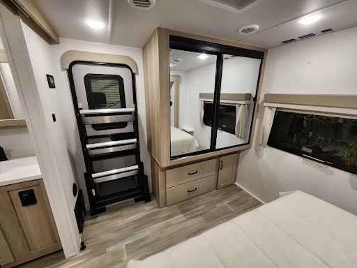 RV rental interior: bedroom features a mirrored wardrobe, comfortable bed, and folding steps beside an interior door.. Forest River Flagstaff 2024