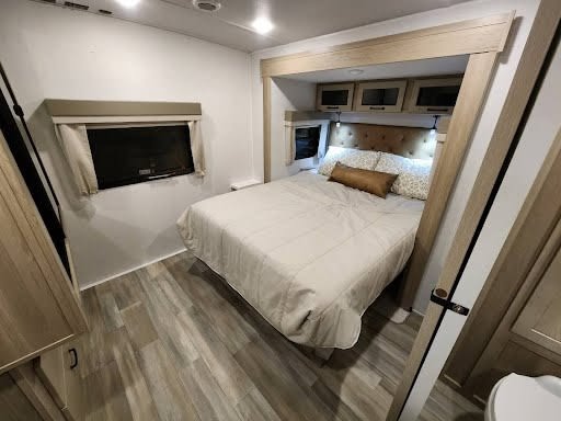 Experience comfort in this RV rental bedroom: cozy bed, lighted headboard, TV, and overhead storage.. Forest River Flagstaff 2024