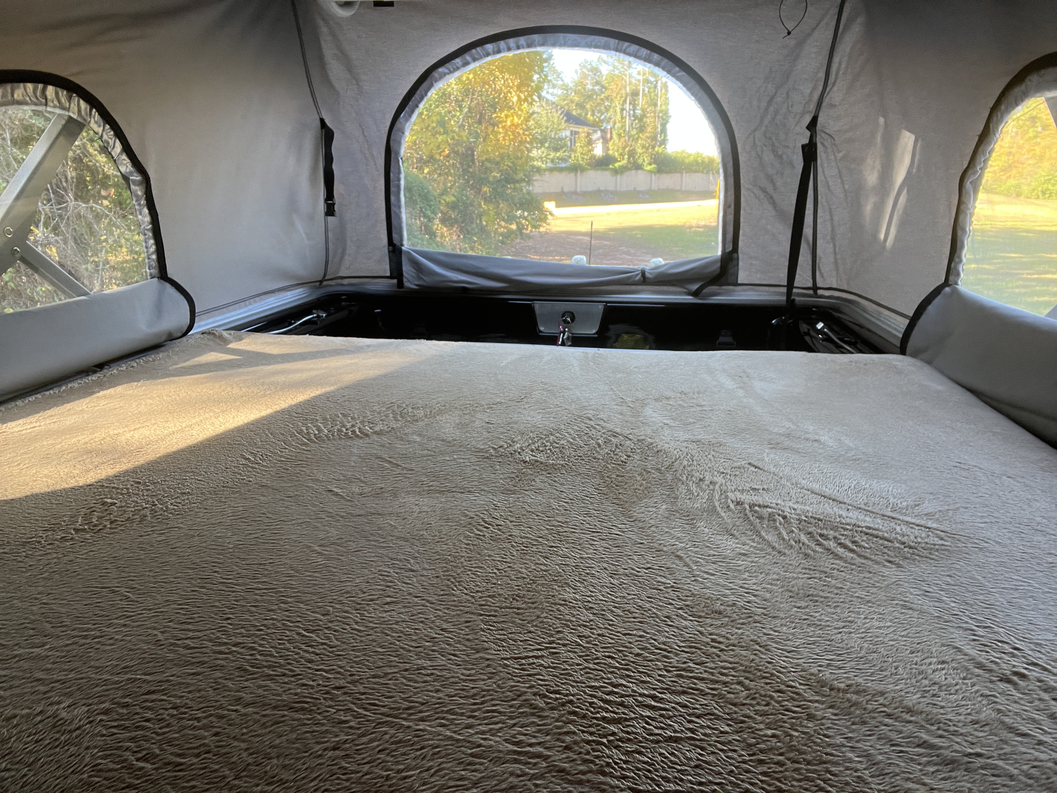 Cozy RV rental interior: soft bed, arched window with a view of trees & a house outside.. Thor Sequence 20A 2021