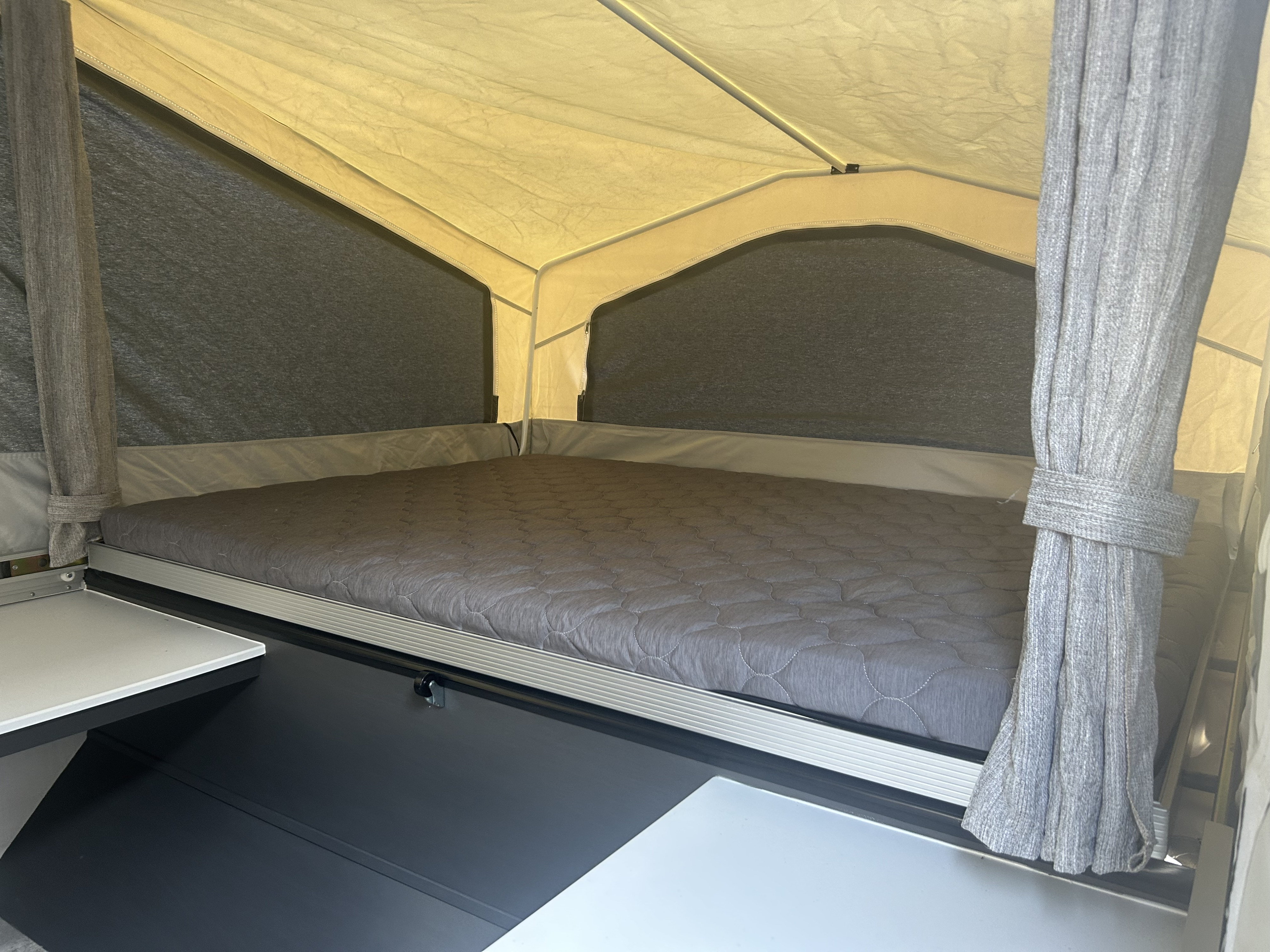 Cozy sleeping area inside an RV rental, featuring a gray quilted mattress, dark fabric walls, and tied-back curtains.. Forest River Flagstaff 2026