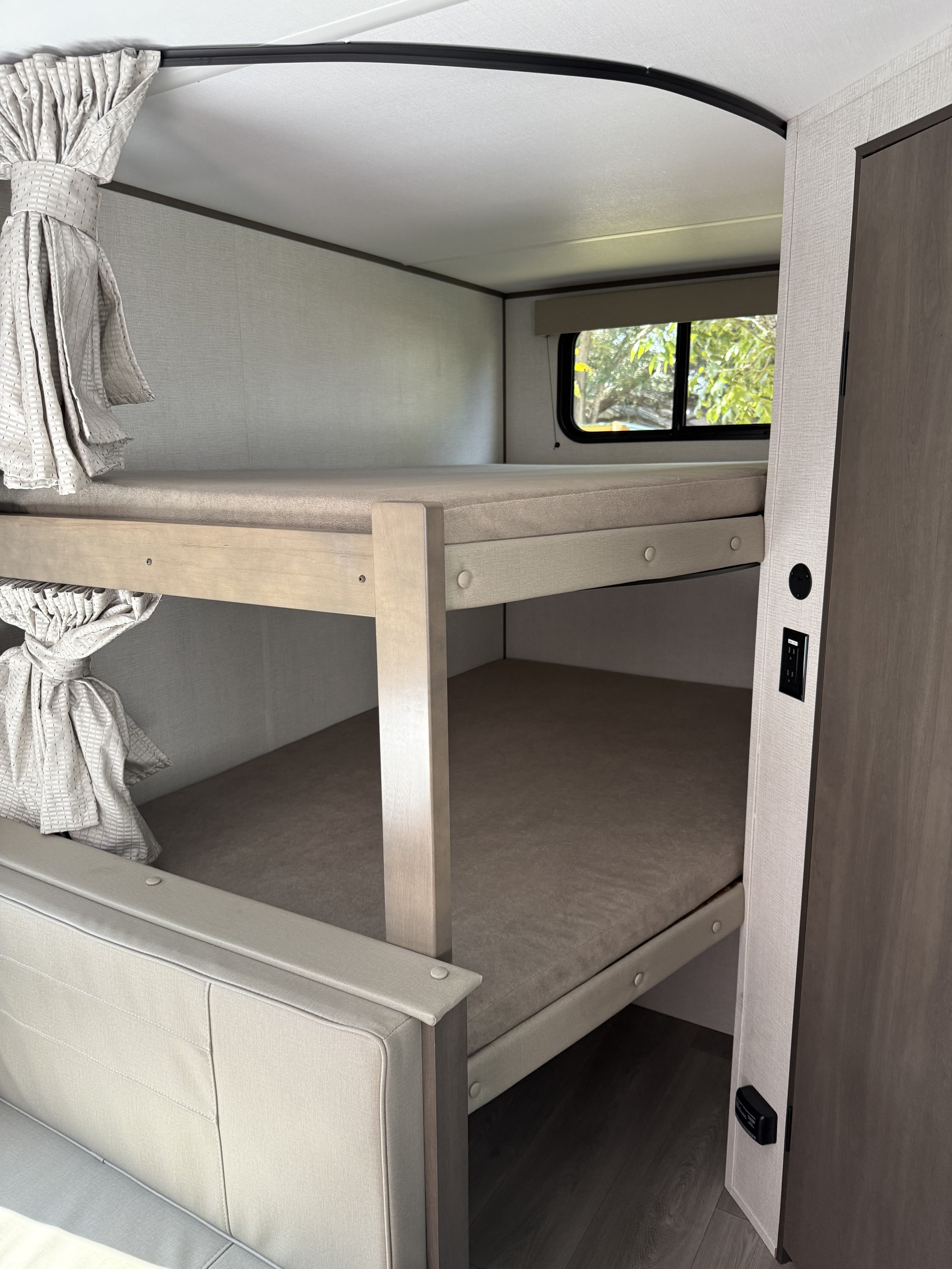 An RV rental's light wood bunk beds with soft mattresses, tied curtains, and a window for views. Perfect for families.. Transcend 26BHX 2025