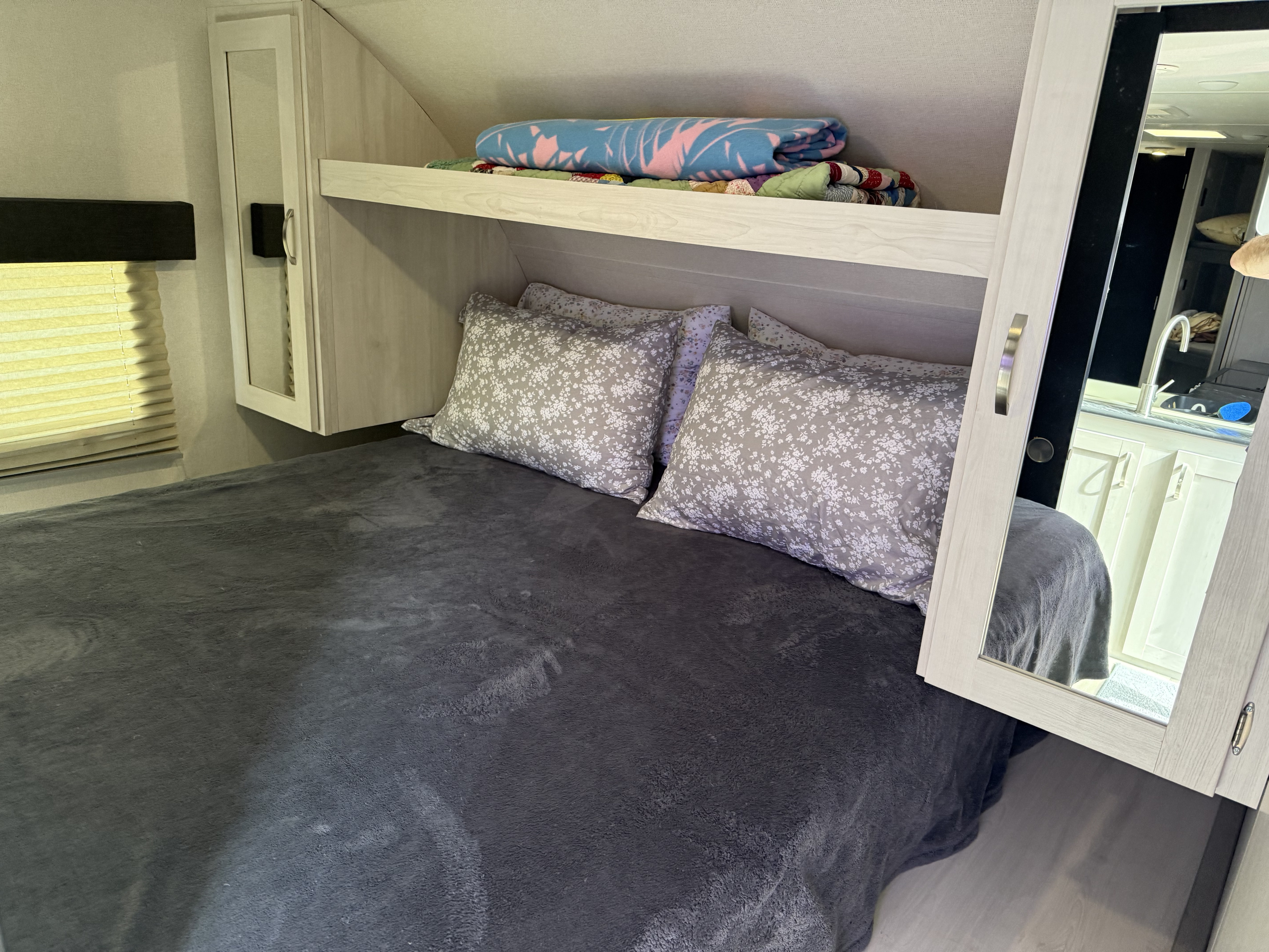 Cozy rv rental bedroom features a bed with patterned pillows, overhead shelf, window, and mirrored cabinet.. Forest River Tracer LE 2022