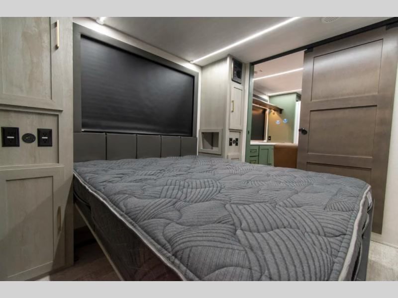 This RV rental bedroom features a comfortable gray bed, built-in storage, and a sliding door to the living area.. Forest River No Boundaries - RV Suite 1 2024