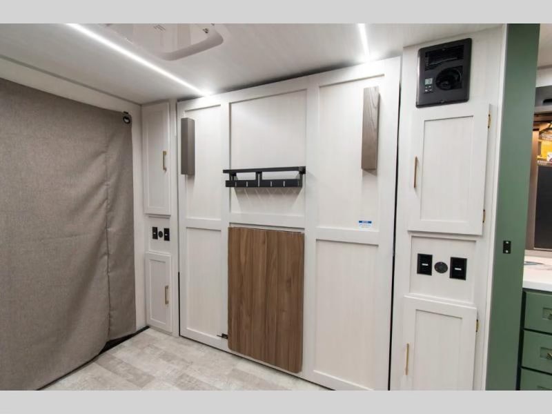 Bright RV rental interior with white cabinets, a folding bed/table, and a privacy curtain, offering compact living space.. Forest River No Boundaries - RV Suite 1 2024