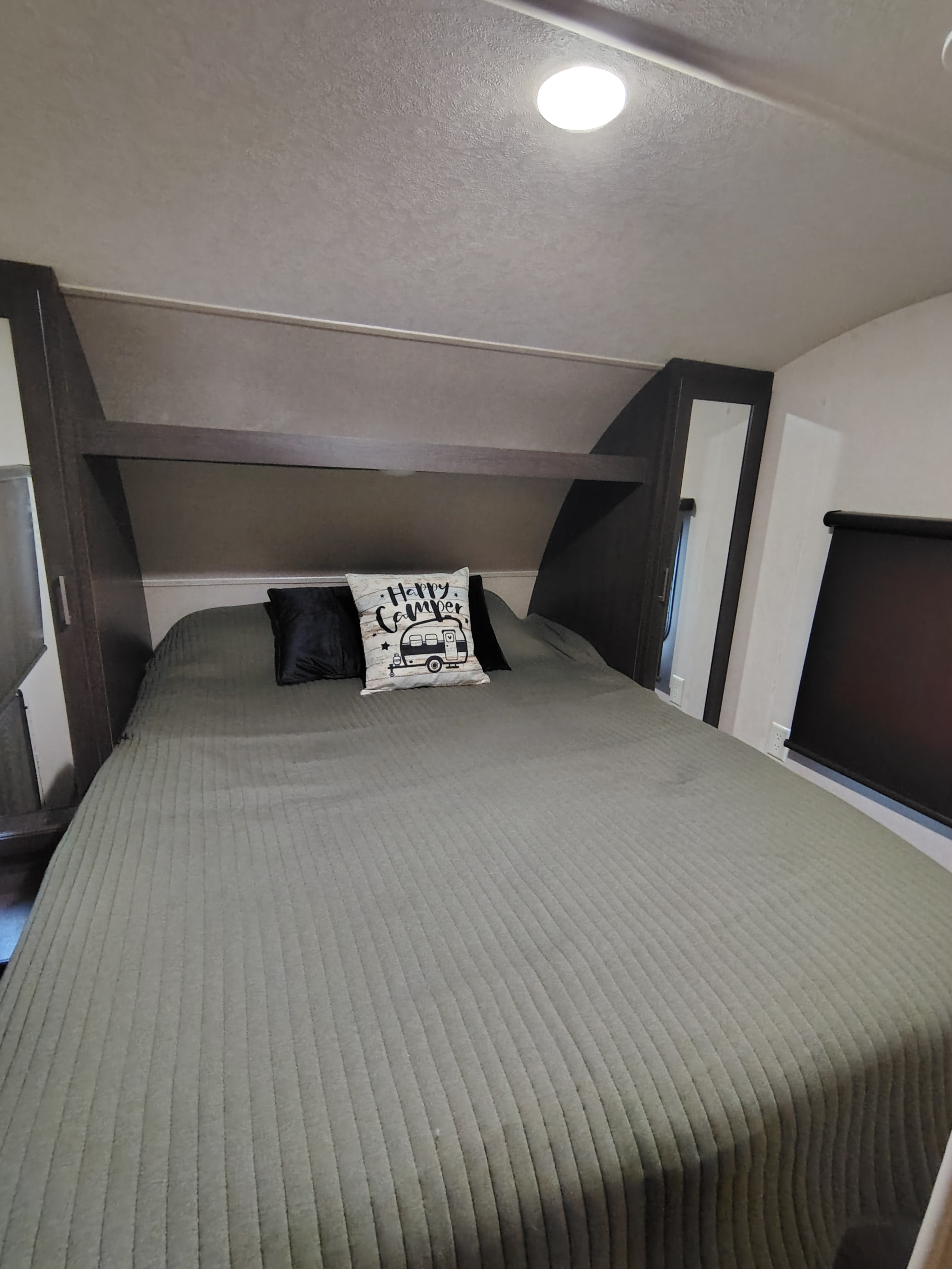 This RV rental bedroom offers a comfortable bed with a 'Happy Camper' pillow and built-in storage.. Forest River Wildwood X-Lite 2019