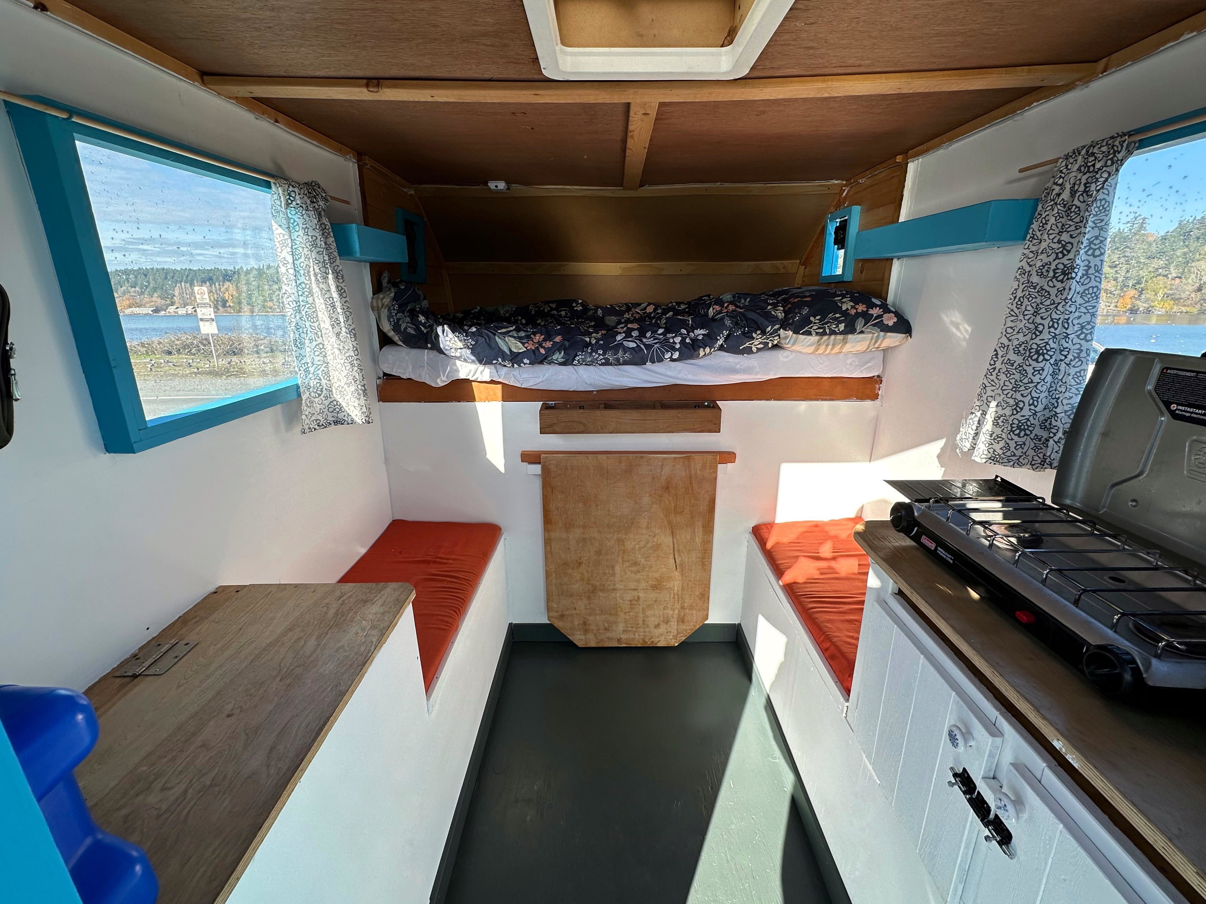 Cozy RV rental camper interior with bed, dinette, portable stove, and window views. Ideal for small space travel.. Dodge 1/2 Ton Hemi 2002