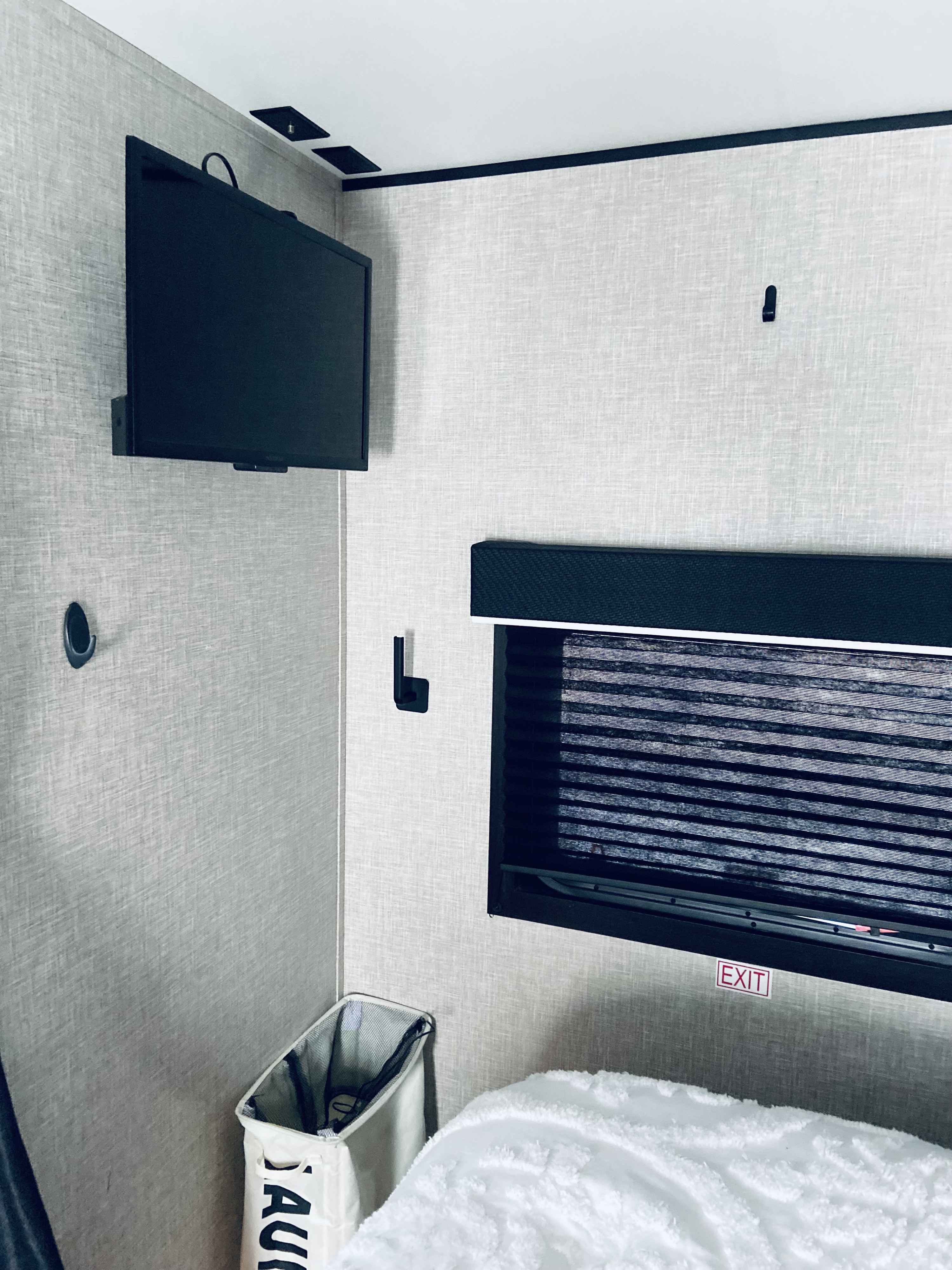 Cozy RV rental bedroom with wall-mounted TV, window with blinds, laundry hamper, and fluffy white bedding.. Jayco Jay Flight 2023