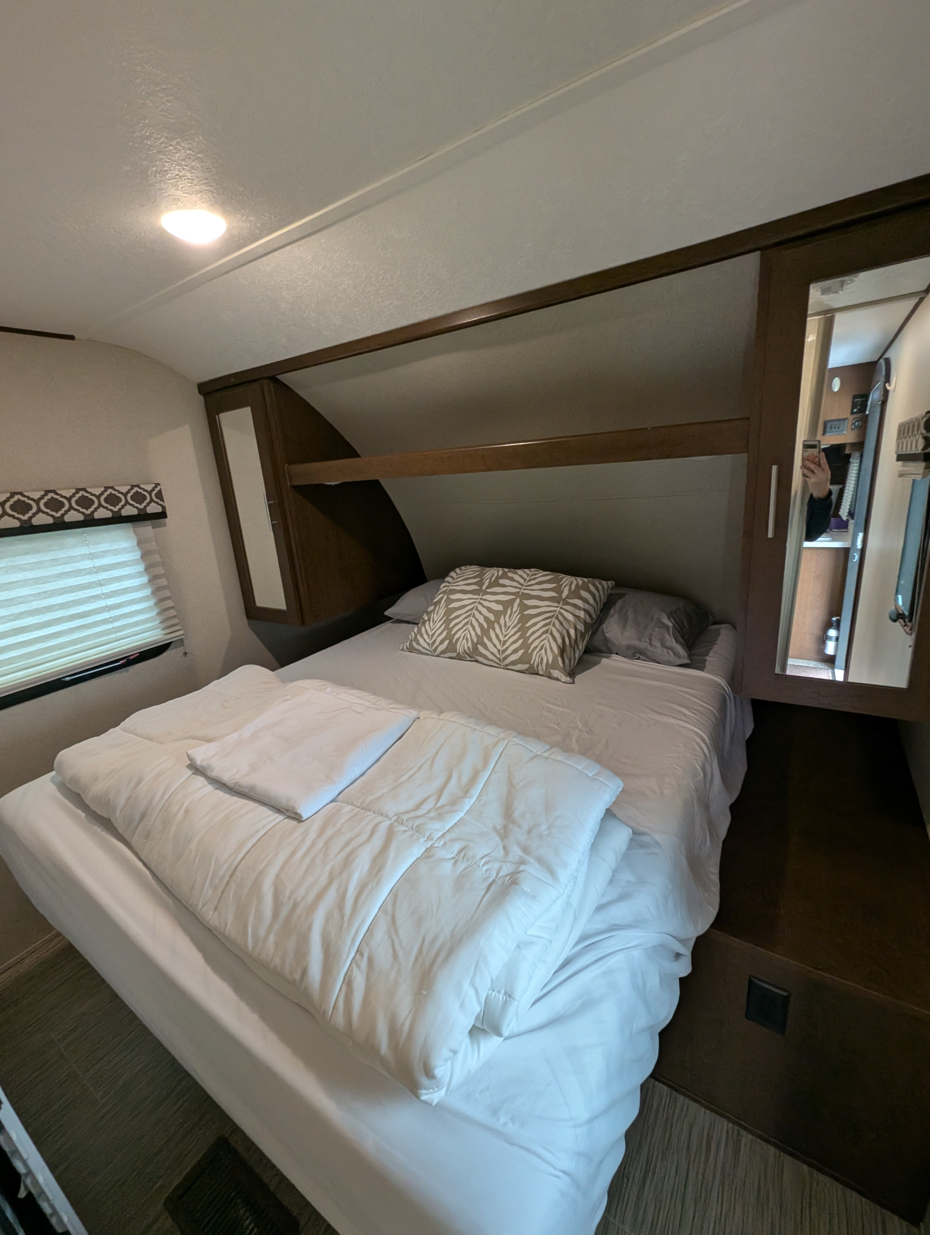 Cozy RV rental bedroom with a comfy bed, overhead storage, and a mirror reflecting a person taking the photo.. Forest River Tracer Breeze 2018