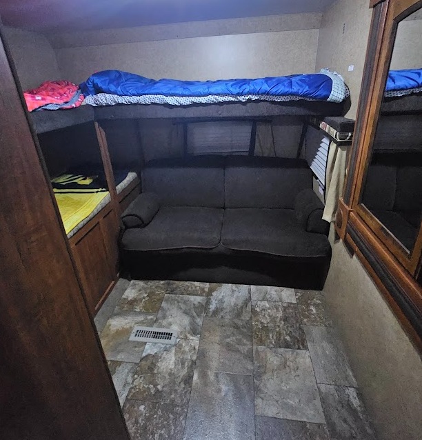 Cozy RV rental bunkhouse: dark sofa, bunk beds with bedding, and tiled floor in a compact camper interior.. Jayco White Hawk Ultra Lite 2013