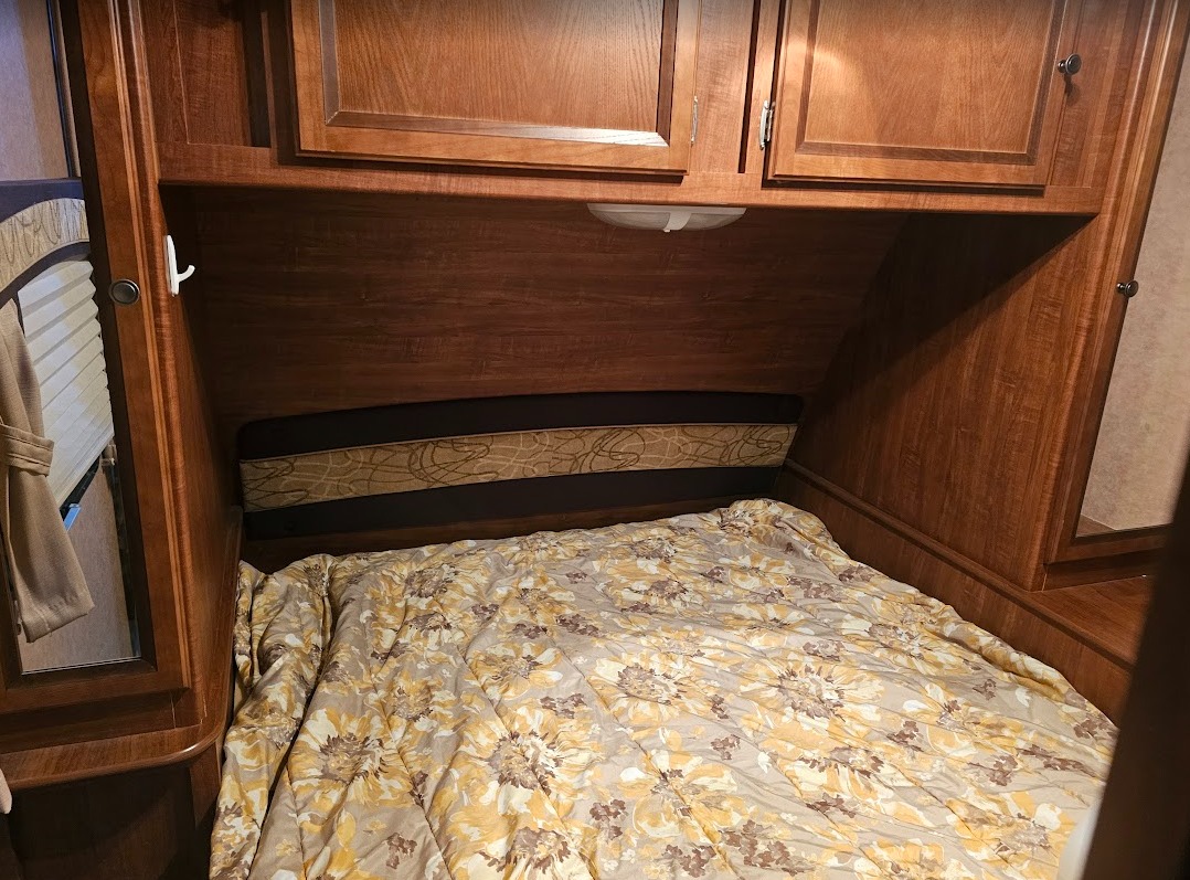 An inviting RV rental bedroom with a floral comforter on the bed, overhead wood cabinets, and an integrated headboard.. Jayco White Hawk Ultra Lite 2013