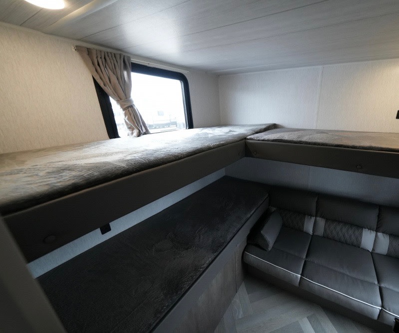 Cozy RV rental interior featuring bunk beds, a window with curtains, and dark gray sofa seating.. Forest River Wildwood X-Lite 2022