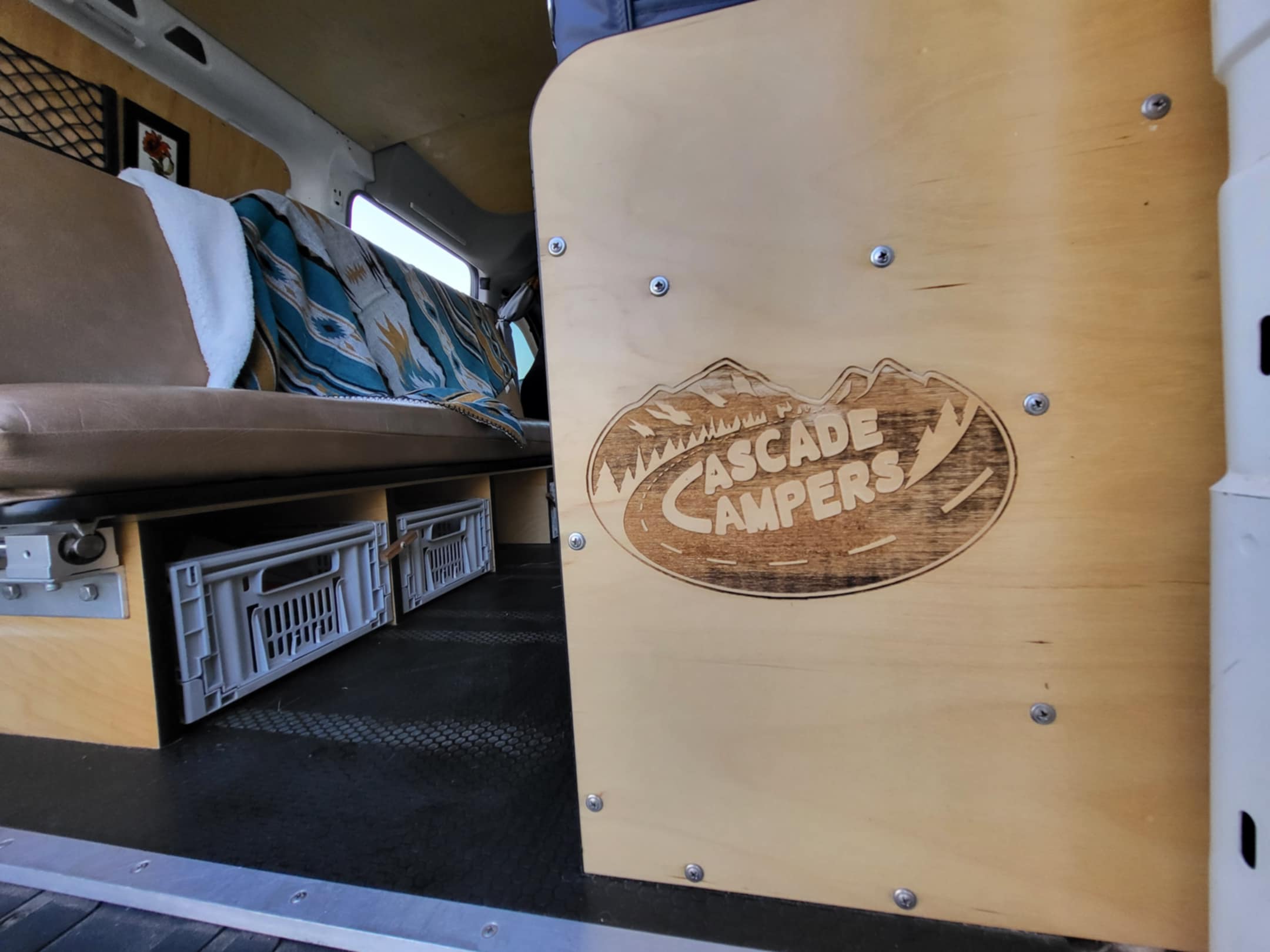 Inside a Cascade Campers RV rental: cozy seating, custom wood paneling with logo, and clever storage crates.. Dodge Dodge Promaster 2019