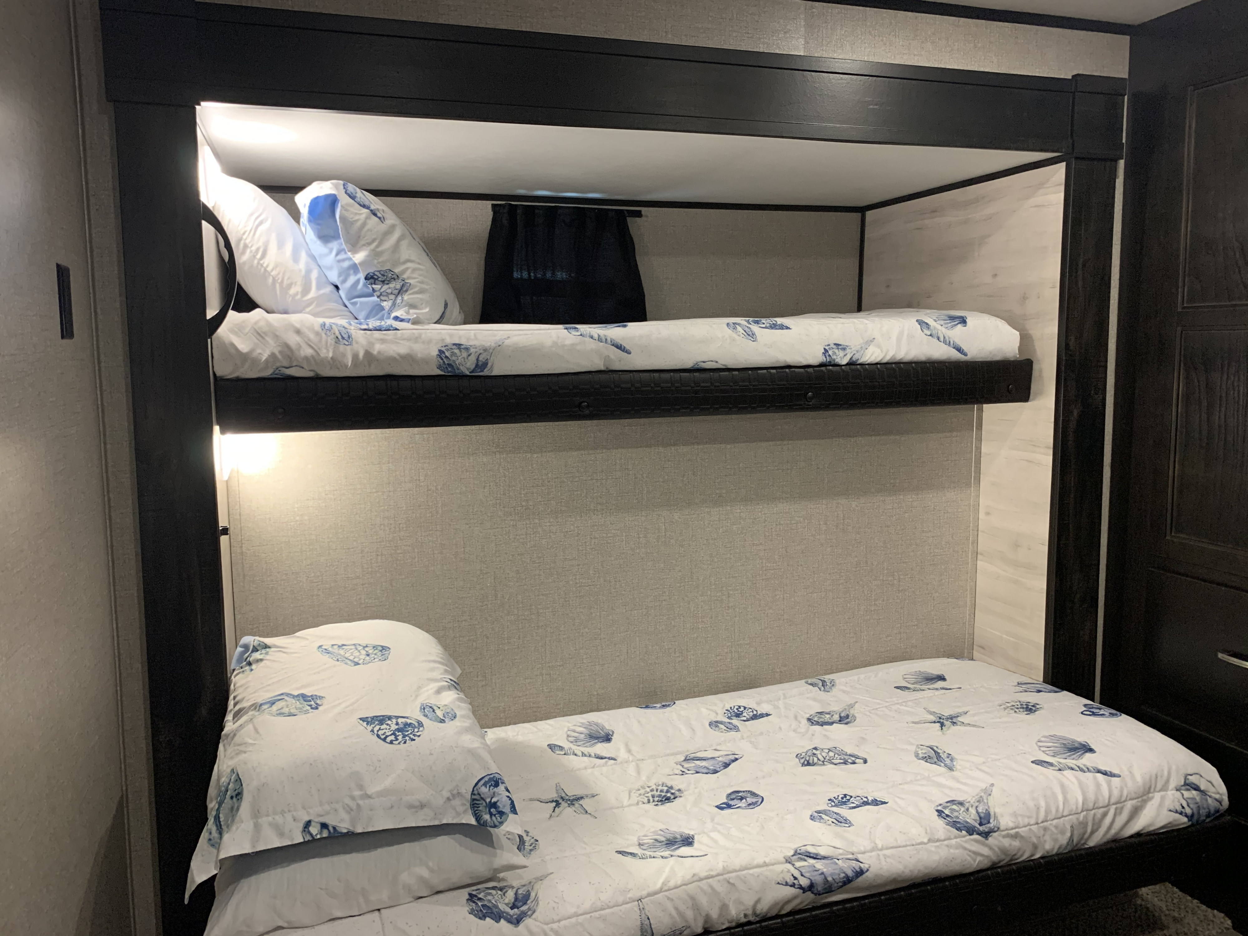 Brightly lit RV rental bunk beds featuring white bedding with blue seashell patterns, set in a compact interior.. Jayco Jay Flight 2021