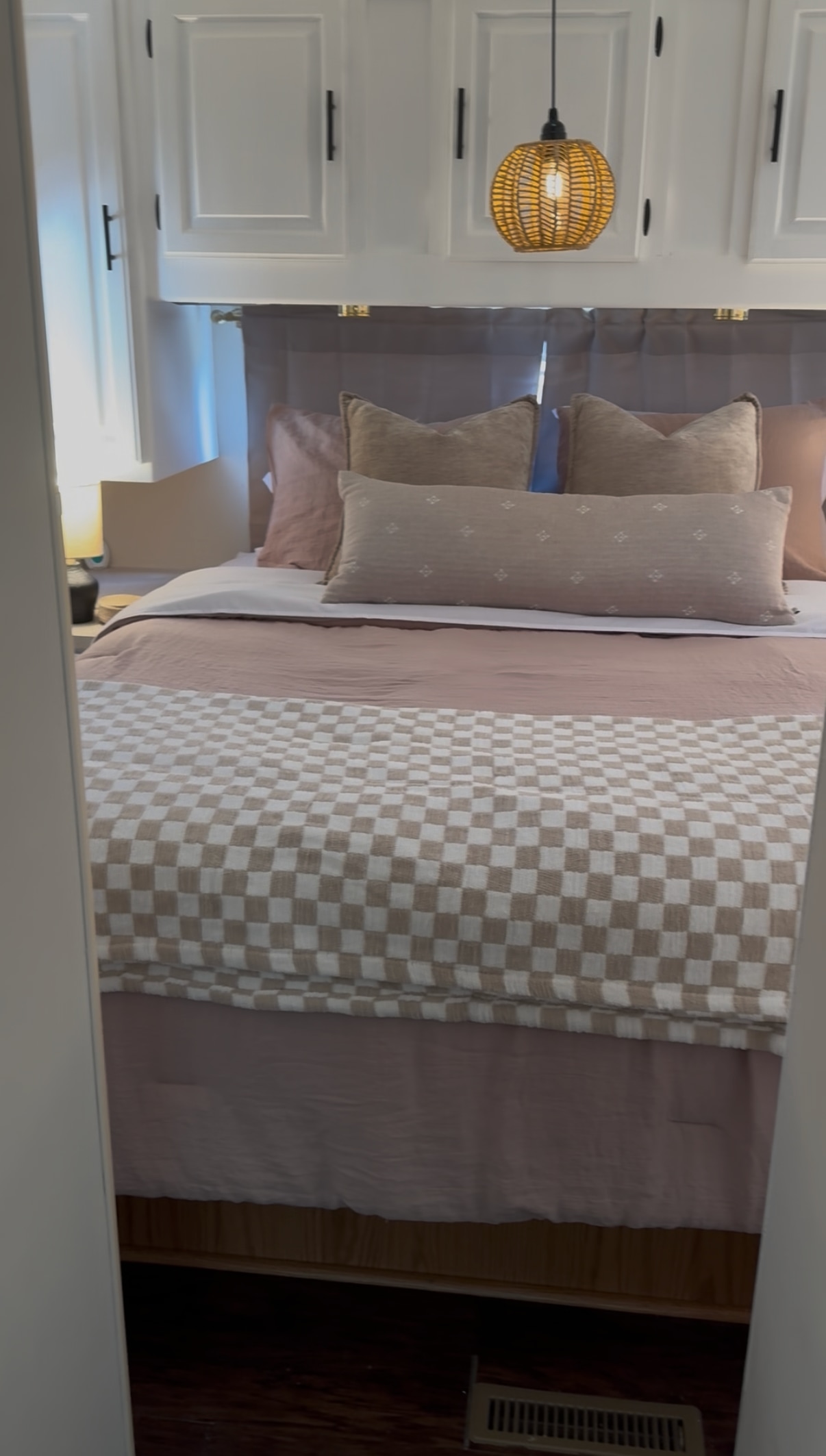 Cozy RV rental bedroom with white overhead cabinets, wicker pendant light, pink duvet, and a checkered throw. Stylish RV interior design.. Ford Jayco Eagle 2001